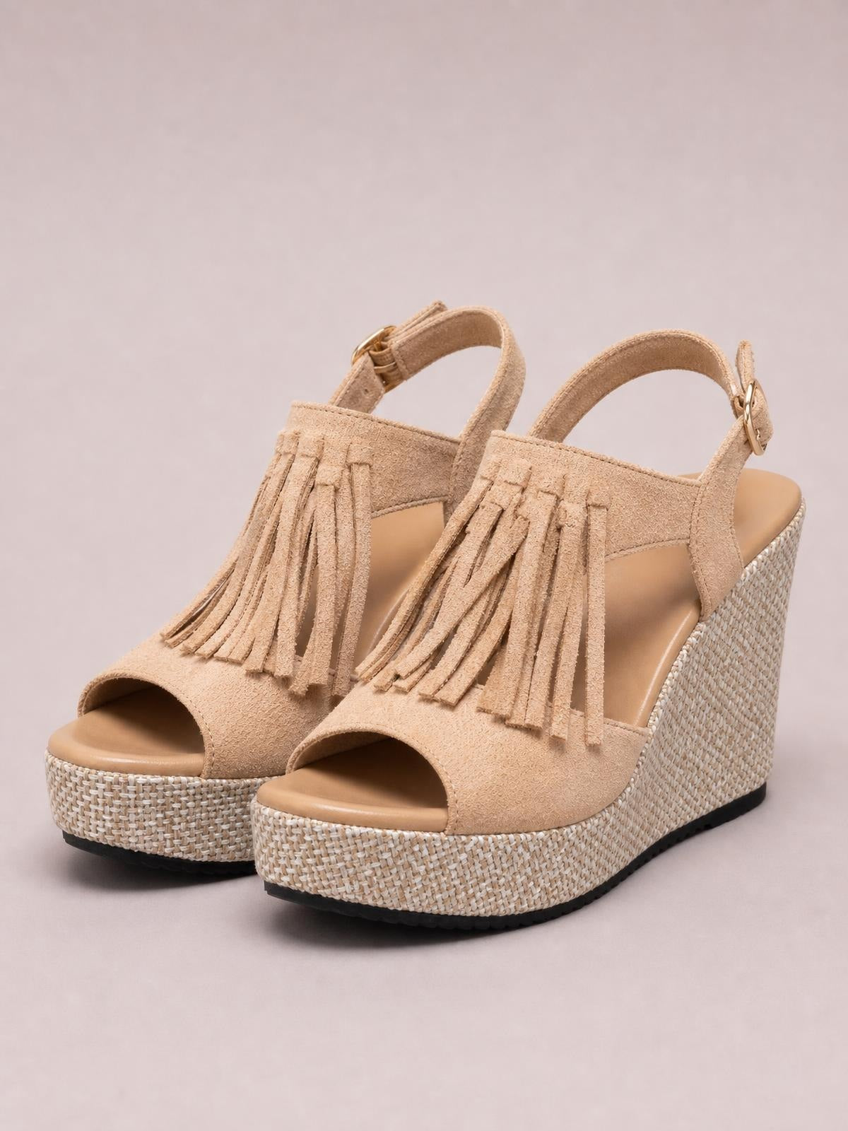 Tan suede peep-toe wedge sandals feature long fringe, ankle buckle straps, woven espadrille-style wedge heels, and black rubber outsoles.
