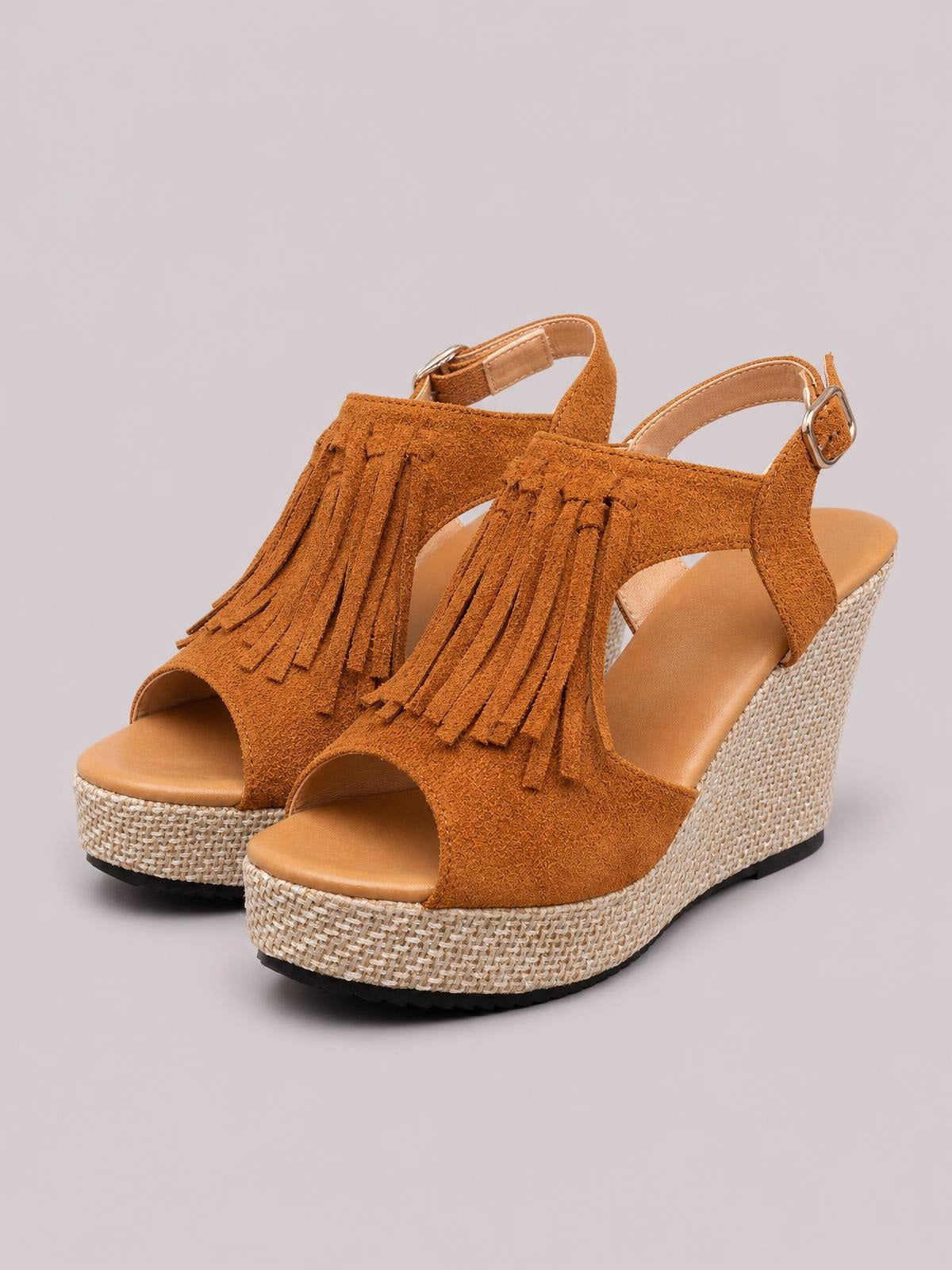 Rust-brown suede wedge sandals feature peep toes, ankle buckle straps, long fringe detailing, and textured woven mid-height wedge heels.