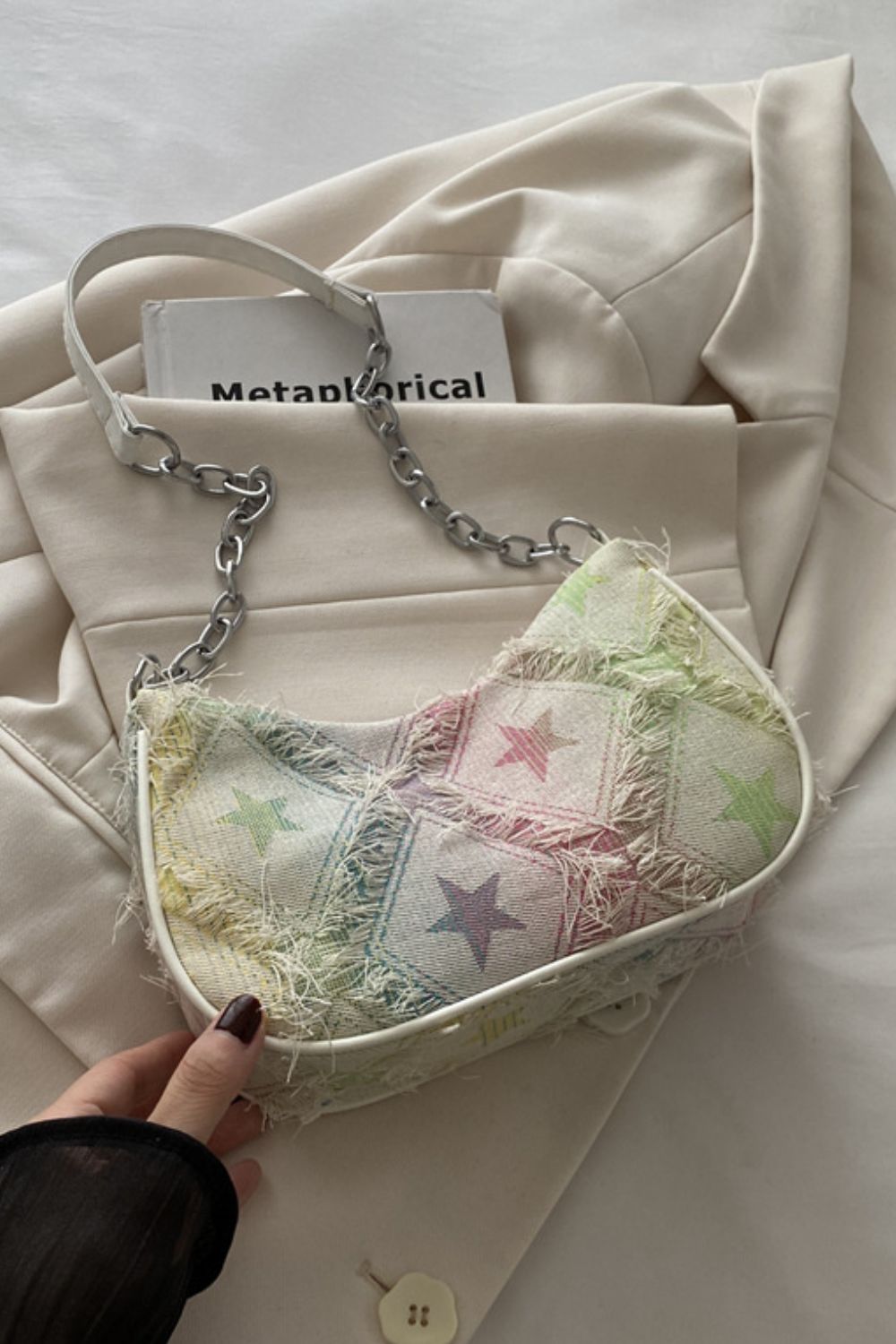 A medium shoulder bag with a softly curved silhouette, multicolor star print, fringed denim texture, and a mixed strap with a chain accent.