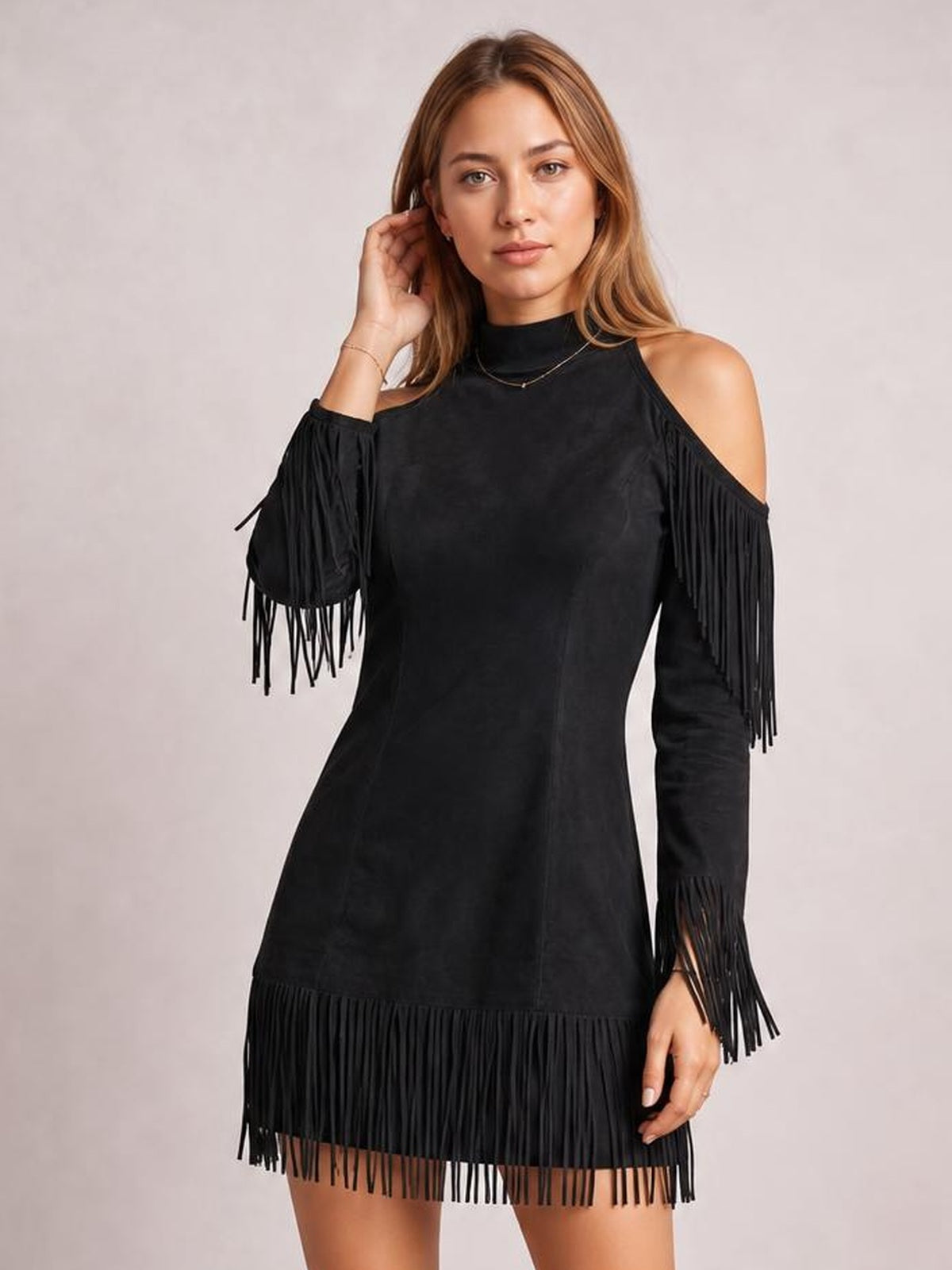 Model poses in a black cold shoulder mini dress with a fitted silhouette, high neckline, long fringe-trimmed sleeves, and a fringe hem.