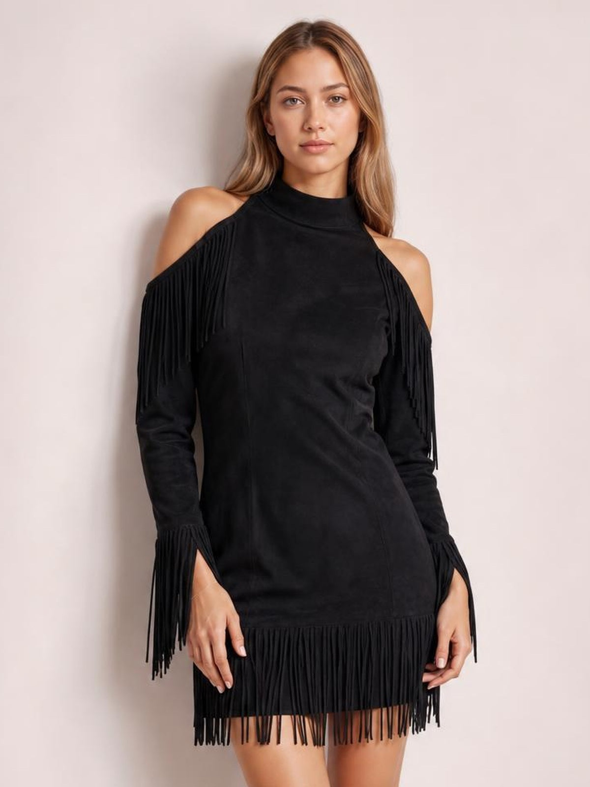 A model stands in a fitted black cold-shoulder mini dress with a high neckline, long sleeves, dramatic fringe trim, and a fringe hem.