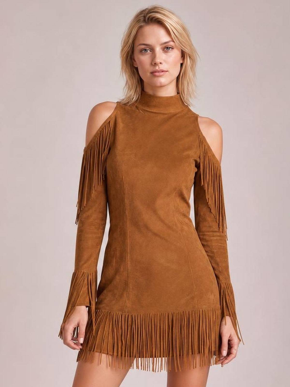 A model stands facing forward in a camel-brown cold shoulder mini dress with a high neck, long sleeves, fitted silhouette, and fringe trim at the shoulders, cuffs, and hem.