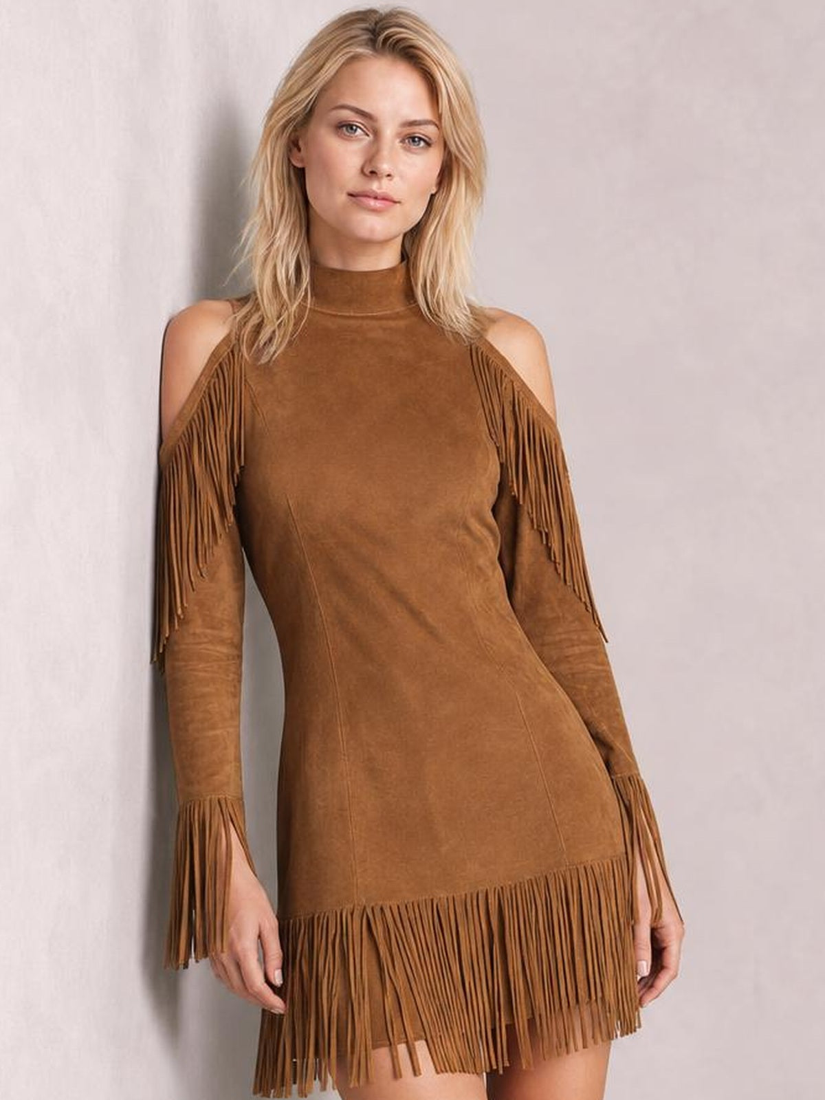 Model leans in a fitted brown cold shoulder mini dress with a high neck, long sleeves, shoulder and cuff fringe, and a dramatic fringed hem.