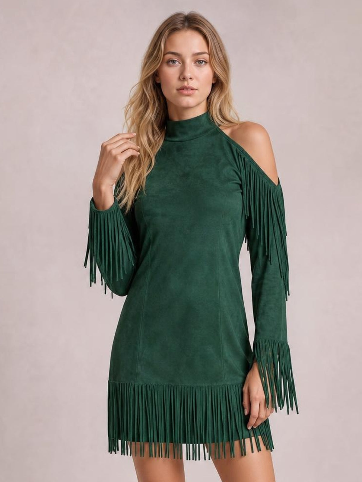 A model poses in a deep green cold shoulder mini dress with a high neckline, long sleeves, fitted silhouette, and fringe trim at the shoulders, cuffs, and hem.
