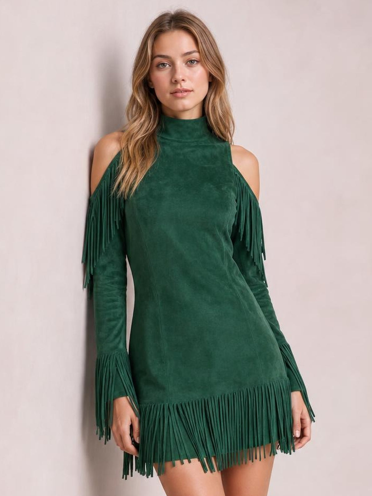 A model poses in a deep green cold-shoulder mini dress with a high neck, long sleeves, straight silhouette, and dramatic fringe at the cuffs and hem.