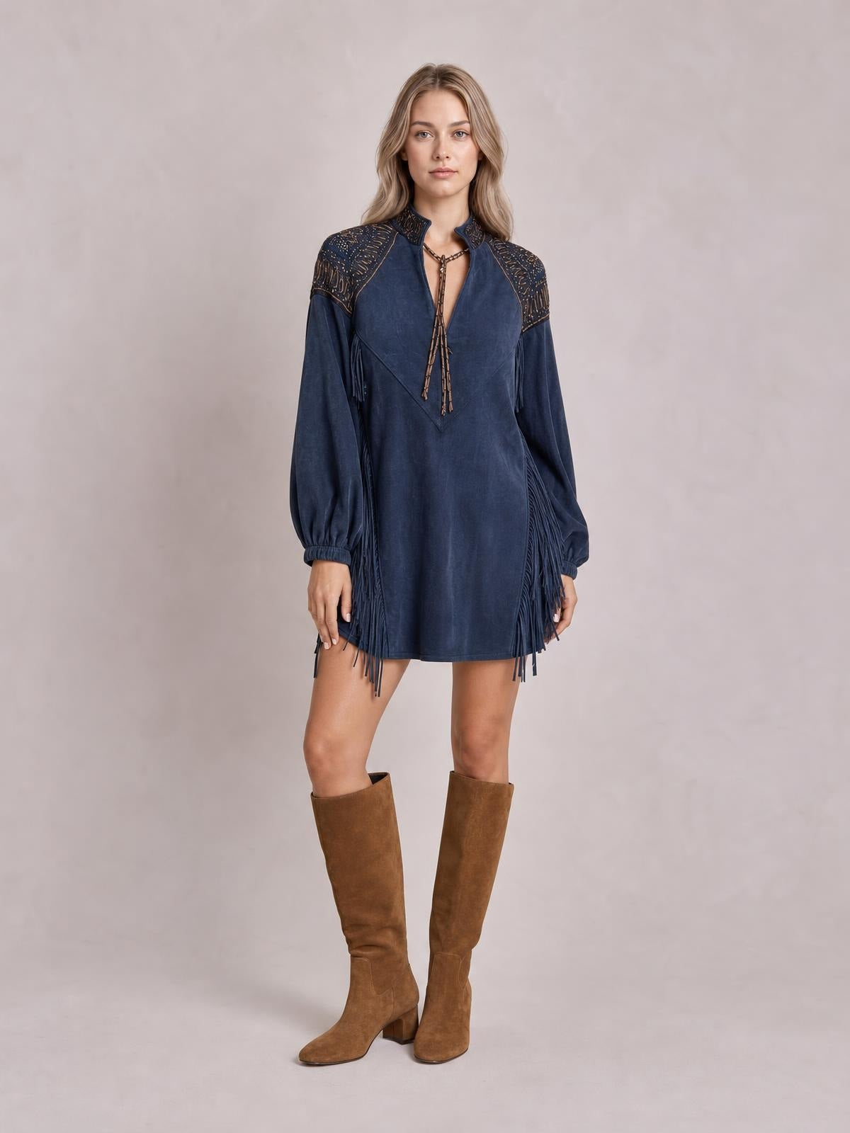 Model stands facing forward in a navy mini dress with lantern sleeves, shoulder detailing, a V-neck tie, and long fringe along the sides and hem.