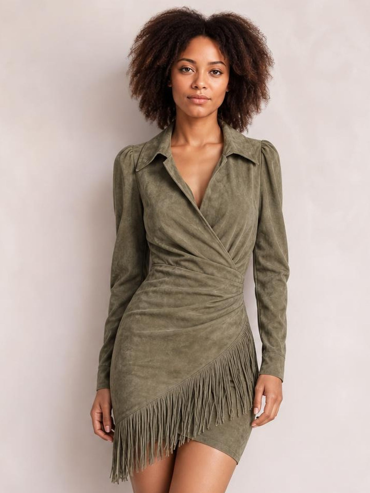 A model poses front-facing in an olive green fringed long sleeve mini dress with a collared wrap bodice, ruched waist, and asymmetrical fringe hem.