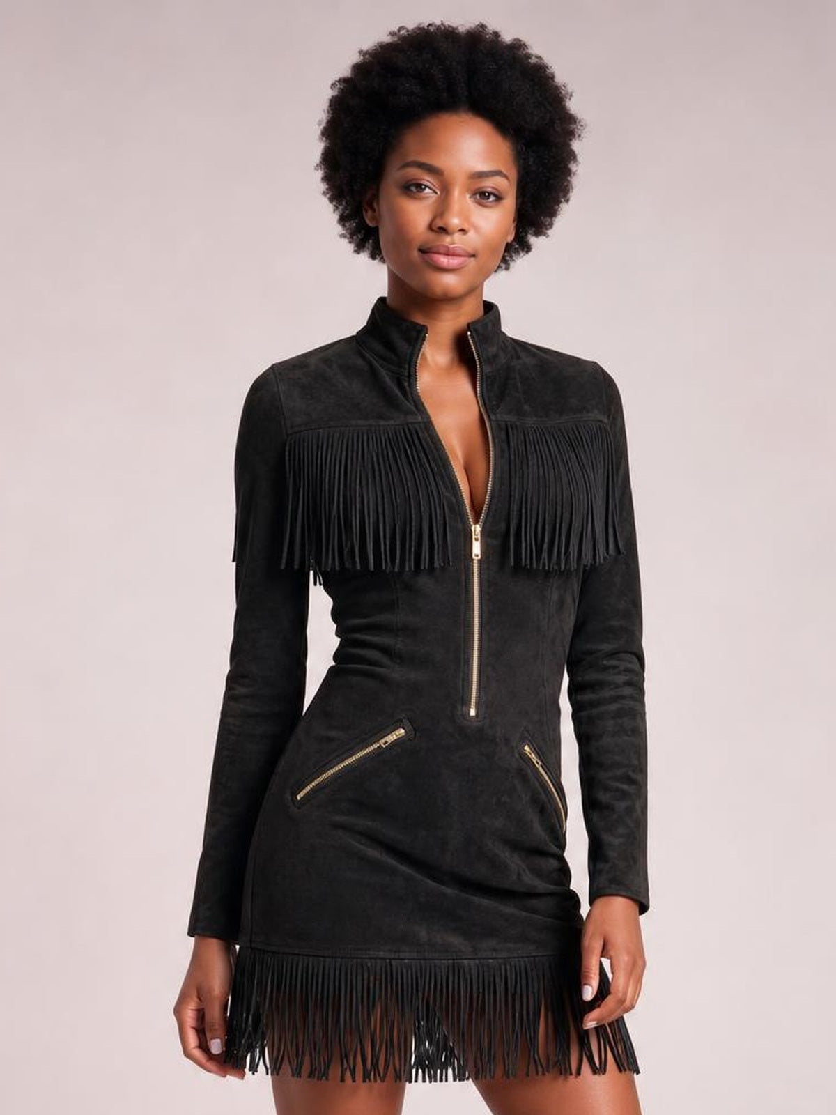 Model stands facing forward in a black long-sleeve mini dress with a zip front, high collar, gold-tone pocket zippers, and fringe across the chest and hem.