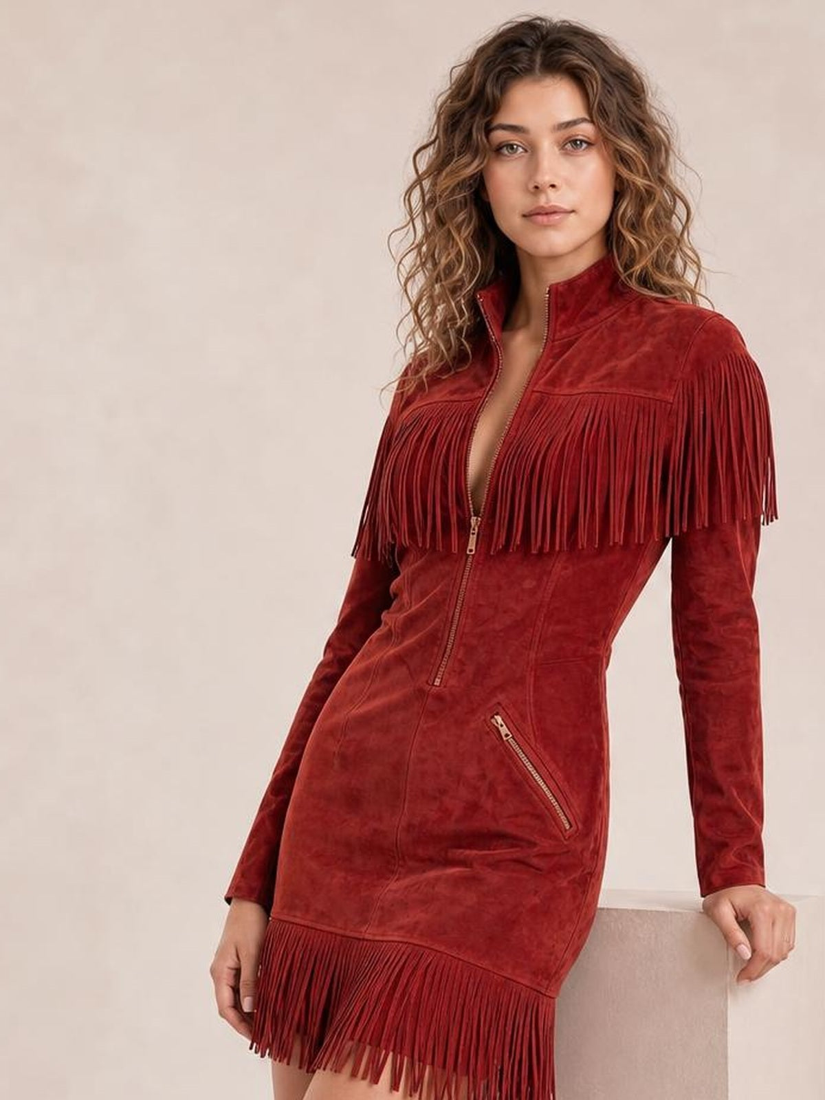 Model poses in a red zip-front mini dress with long sleeves, a fitted silhouette, diagonal zip pockets, and dramatic fringe across the chest and hem.