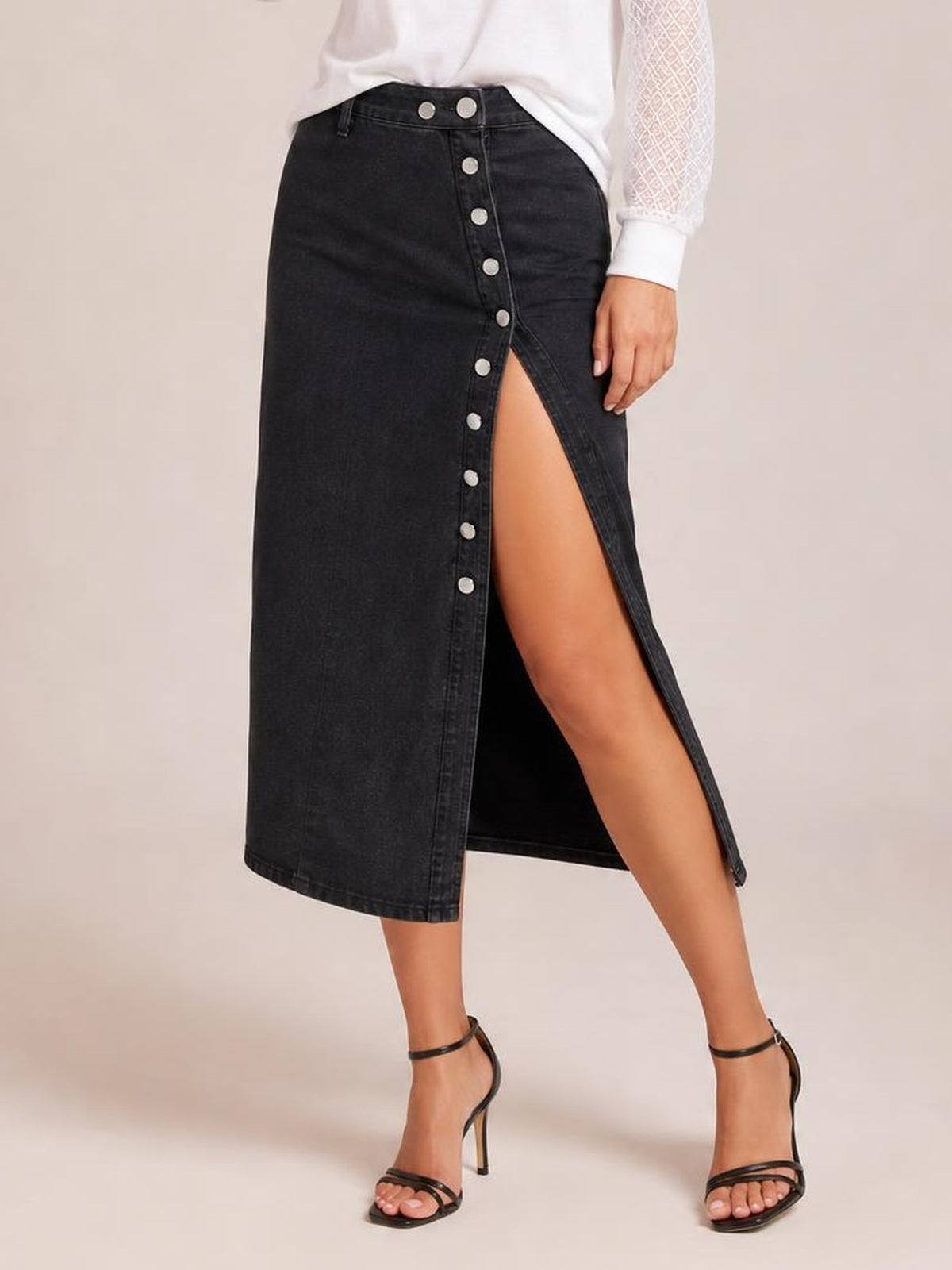 Model poses in a black denim midi skirt with a front button closure, high slit, straight silhouette, and structured seamed construction.