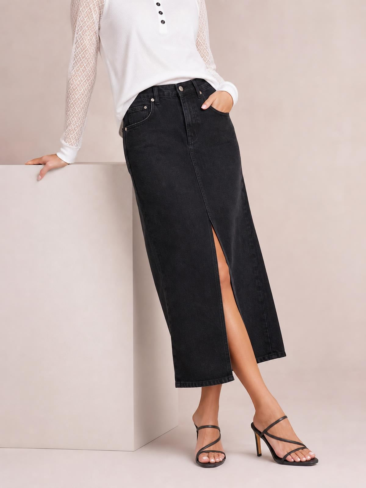 Model wearing a black front-button midi denim skirt with belt loops, five-pocket styling, a straight silhouette, and a front slit.