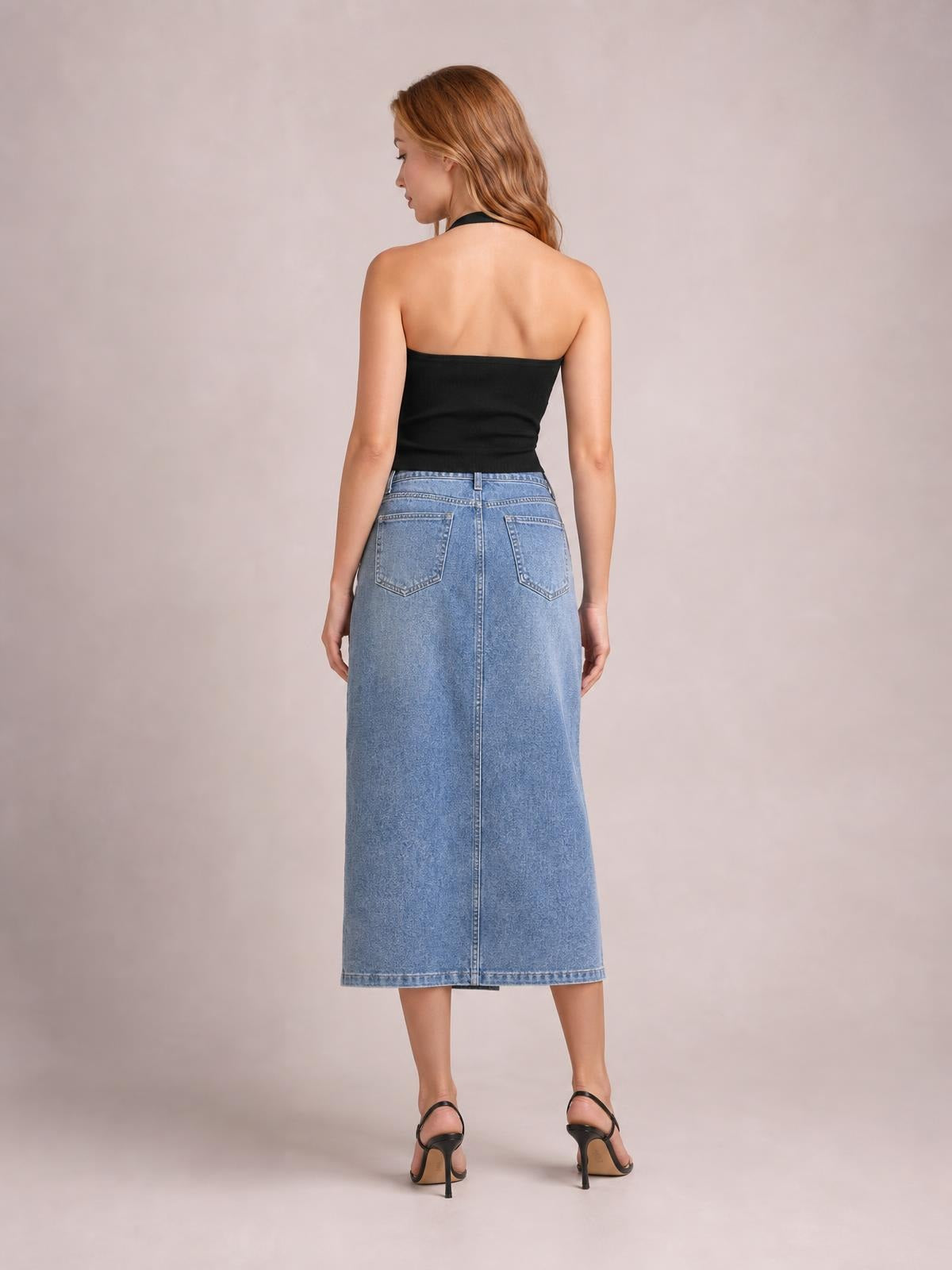 Model shown from behind wearing a light-blue denim midi skirt with a straight silhouette, waistband, belt loops, back patch pockets, and center seam.