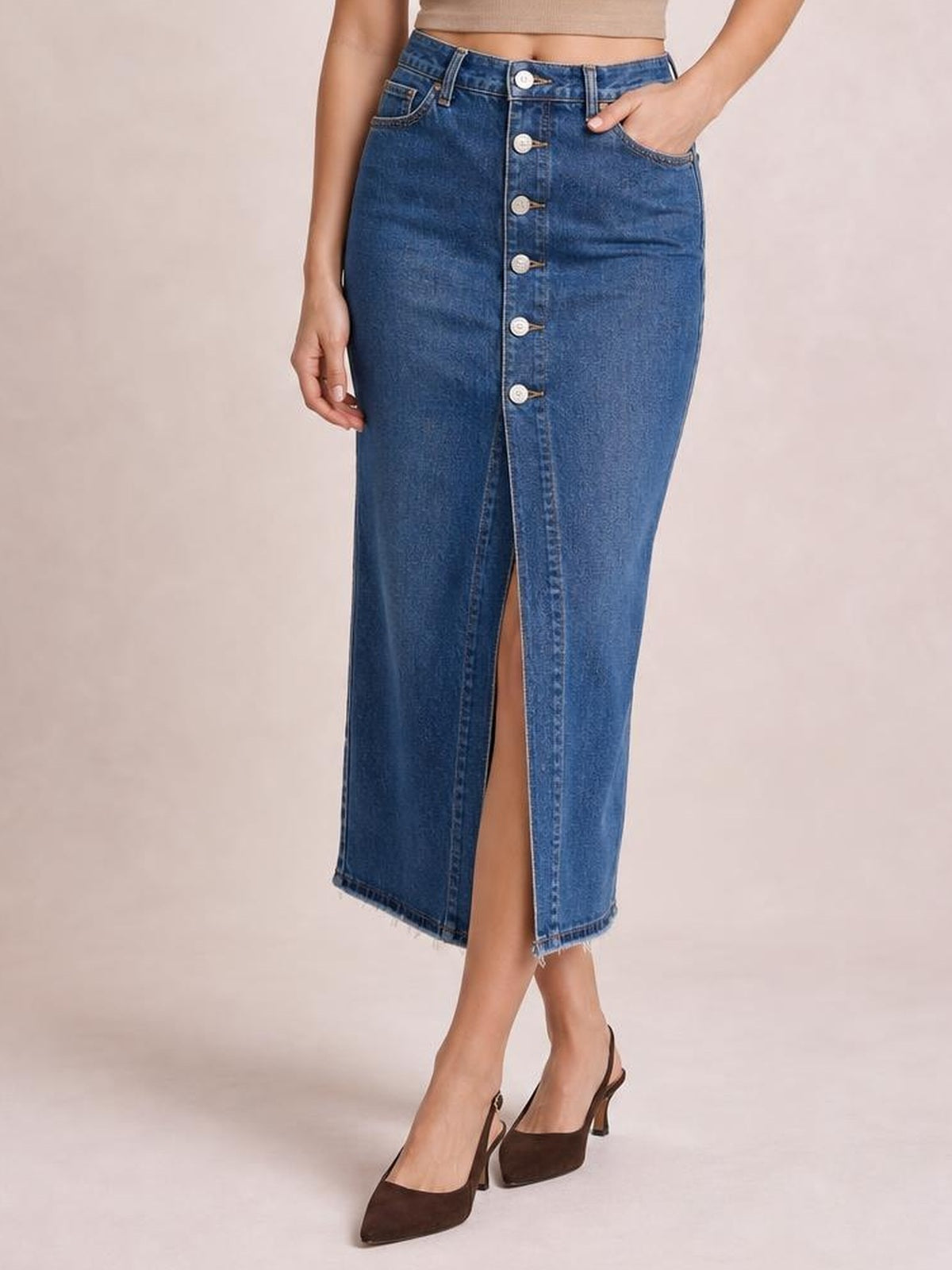 Model poses in a blue denim midi skirt with a front button closure, center slit, fitted silhouette, belt loops, and front pockets.