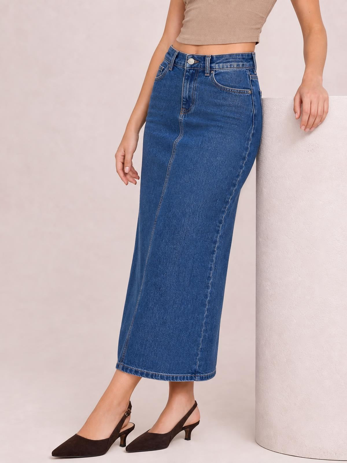 Model wears a blue denim midi skirt with a high waist, front button closure, belt loops, curved pockets, contrast stitching, and a straight silhouette.