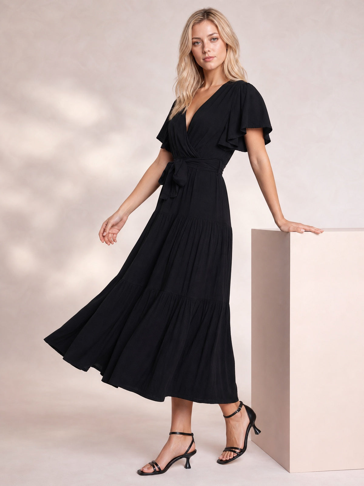 Model poses in a black Front Tie Short Sleeve Tiered Midi Dress with a V-neckline, flutter sleeves, defined waist, and flowing tiered skirt.