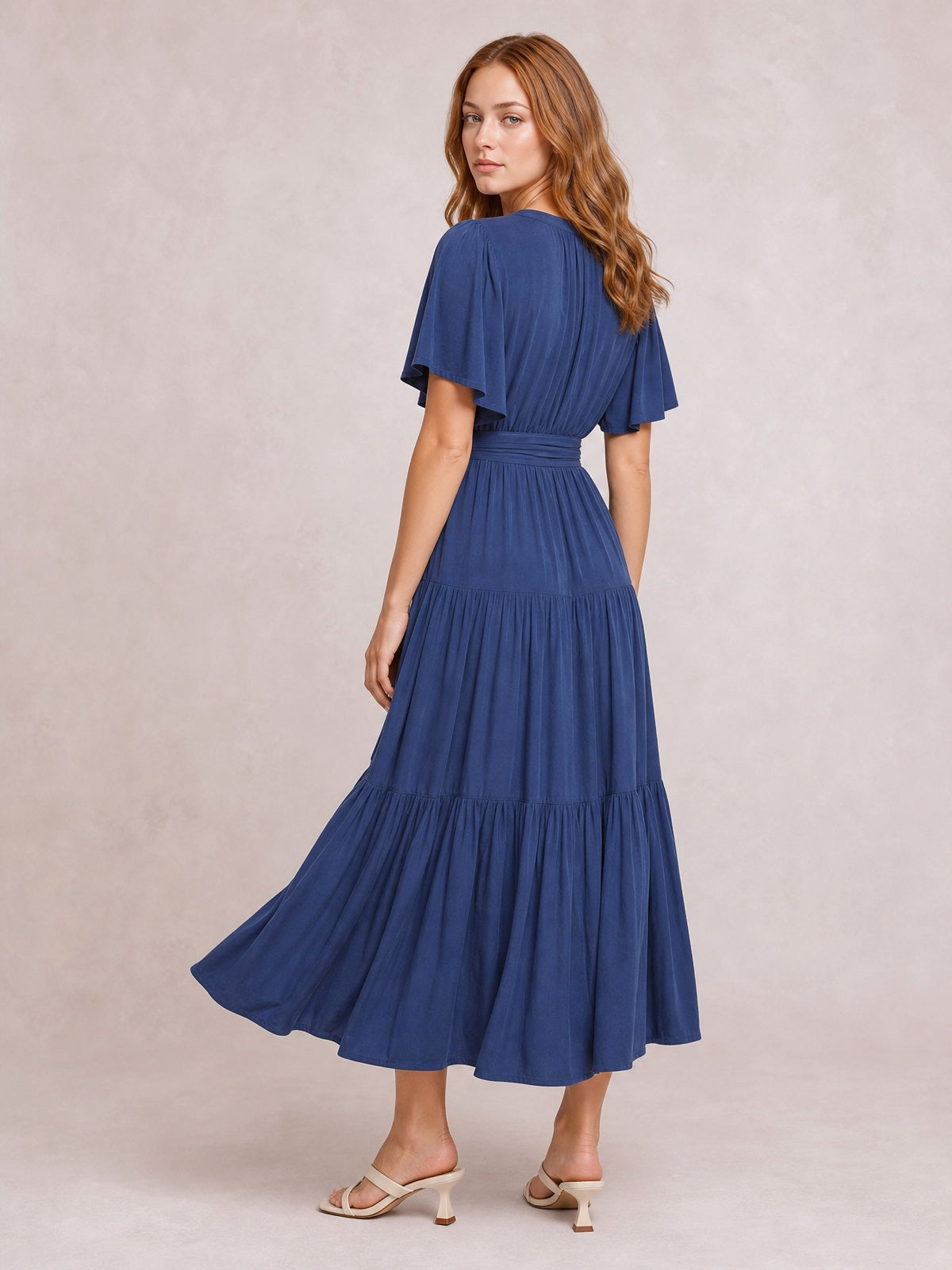 Model poses in a navy blue tiered midi dress with flutter short sleeves, a defined waist, gathered skirt panels, and a flowing flared silhouette.