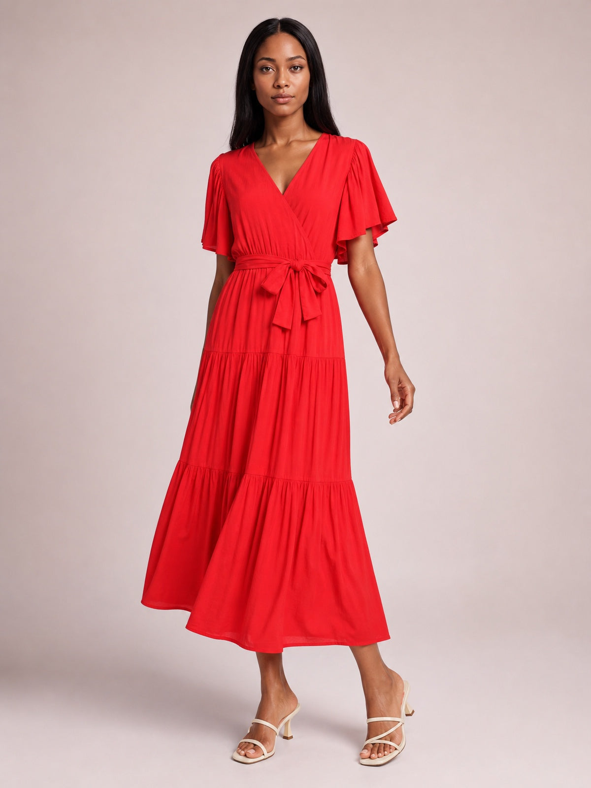 Model wearing a red front-tie midi dress with a V-neckline, flutter short sleeves, gathered waist, and flowing tiered skirt.