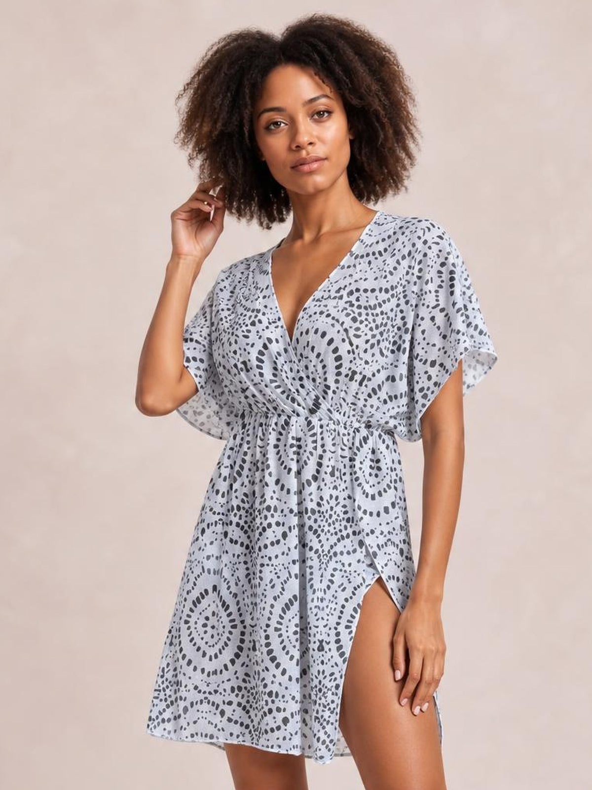 A model poses in a light gray boho print surplice beach cover-up dress with flutter sleeves, a cinched waist, flowing silhouette, and side slit.