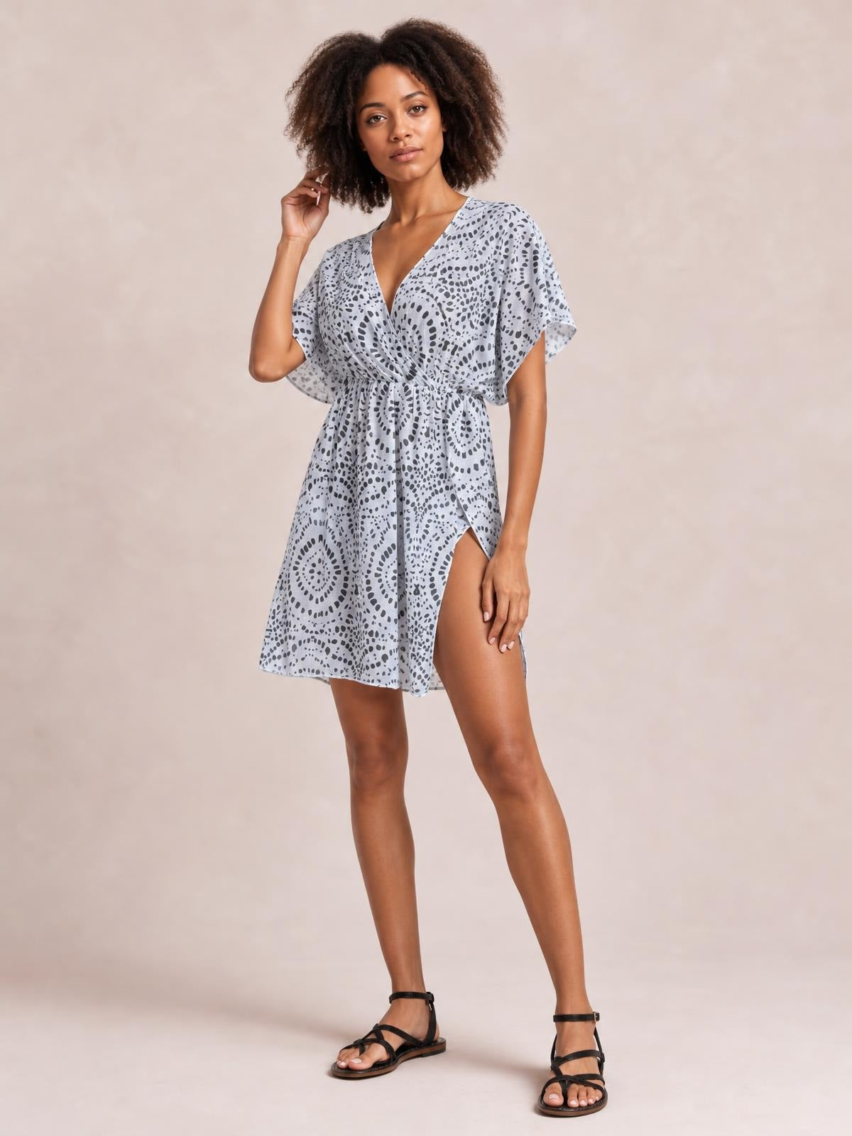 Model poses in a light blue boho print surplice beach cover-up dress with flutter sleeves, a cinched waist, relaxed silhouette, and thigh-high slit.