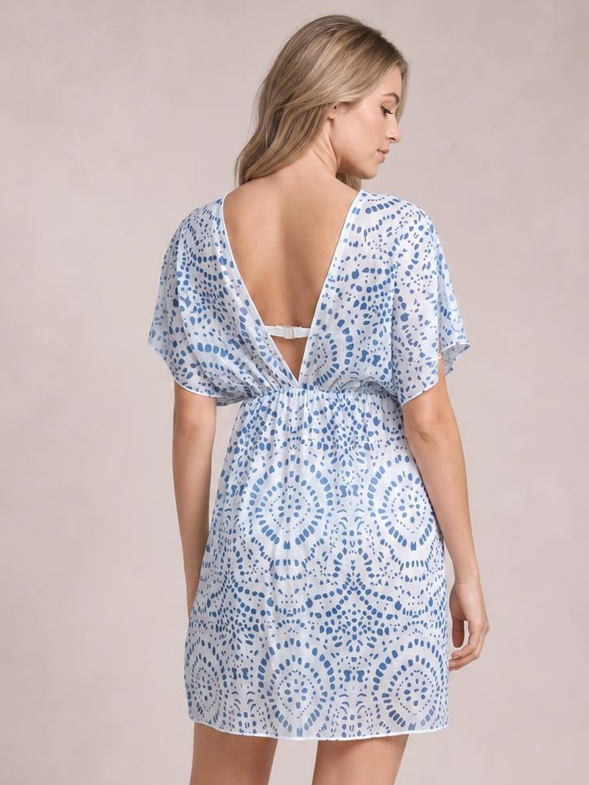 Model turned away wears a blue and white boho print beach cover up dress with short sleeves, a back cutout, waist tie, and relaxed silhouette.