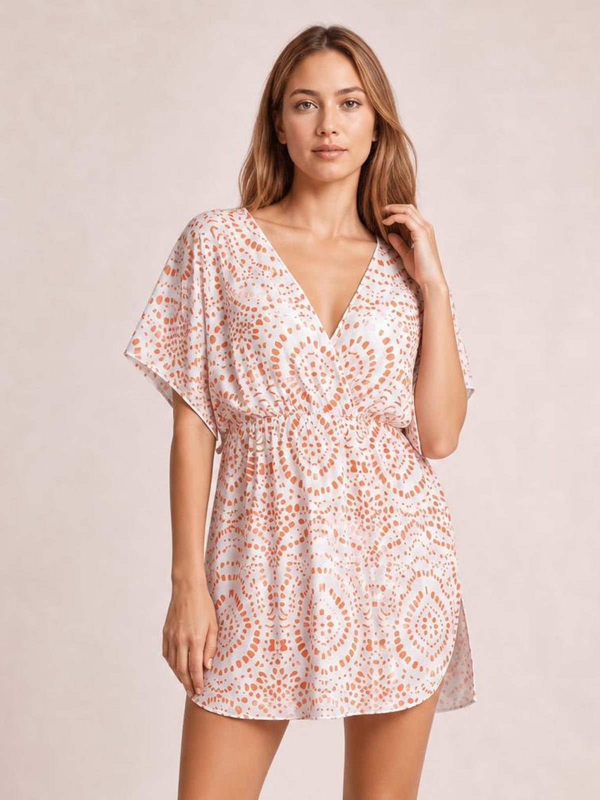 A model poses in a white boho print beach cover-up dress with orange motifs, a surplice V-neck, flutter sleeves, gathered waist, and short flowing silhouette.
