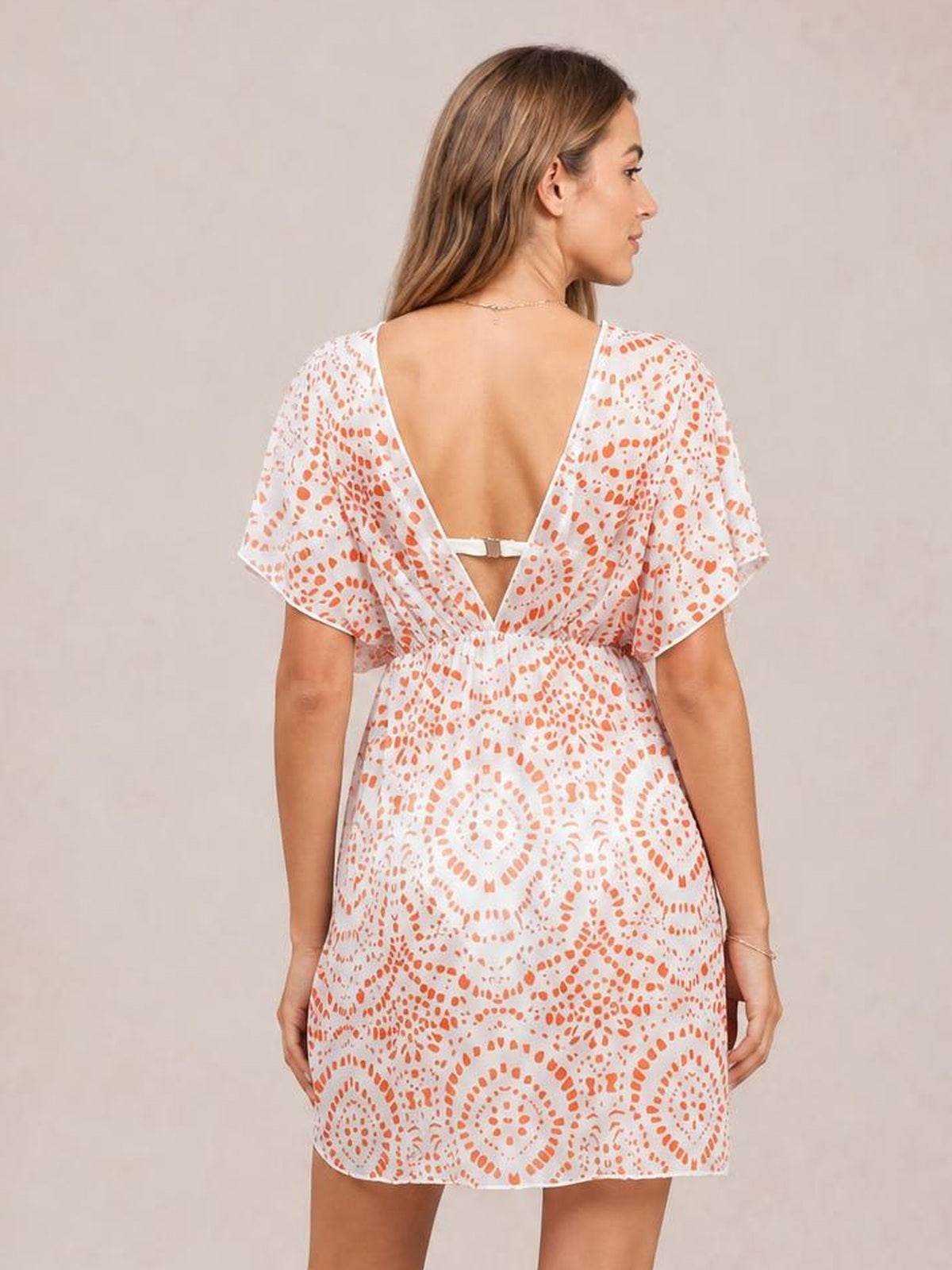 Model shown from behind in a white boho print beach cover-up dress with orange patterning, short flutter sleeves, a deep surplice back, and relaxed silhouette.