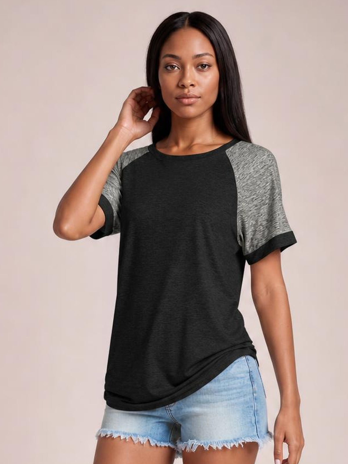 Model poses in a black contrast round-neck short-sleeve T-shirt with gray raglan-style sleeves, black cuffs, and a relaxed longer silhouette.