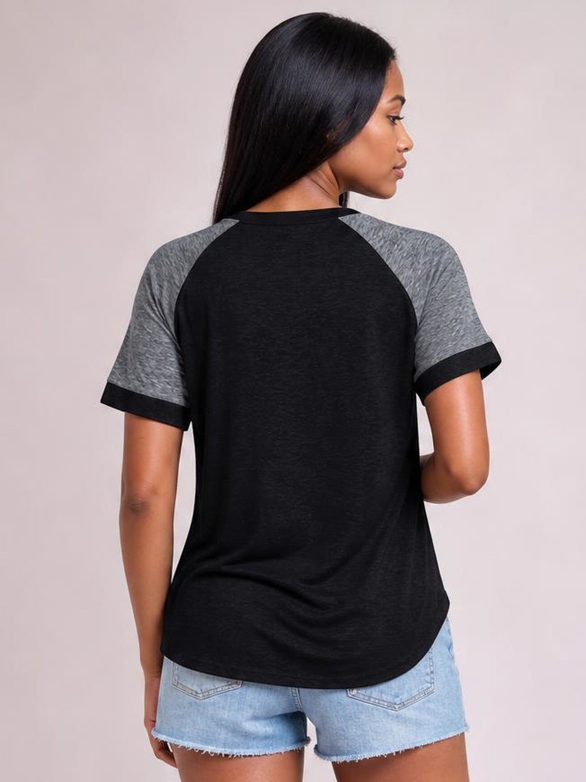 A model shown from the back wears a black contrast round neck short sleeve T-shirt with gray raglan sleeves, black cuffs, and a relaxed curved hem.