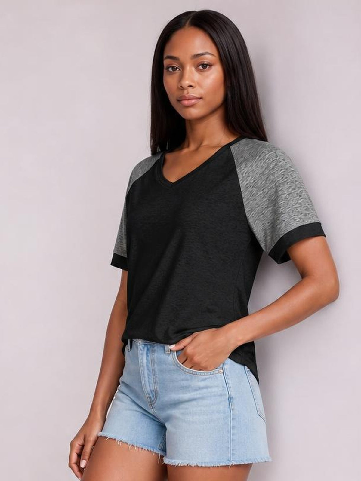 Model poses in a black and gray contrast short sleeve T-shirt with a round neck, relaxed silhouette, and ribbed sleeve cuffs, paired with denim shorts.