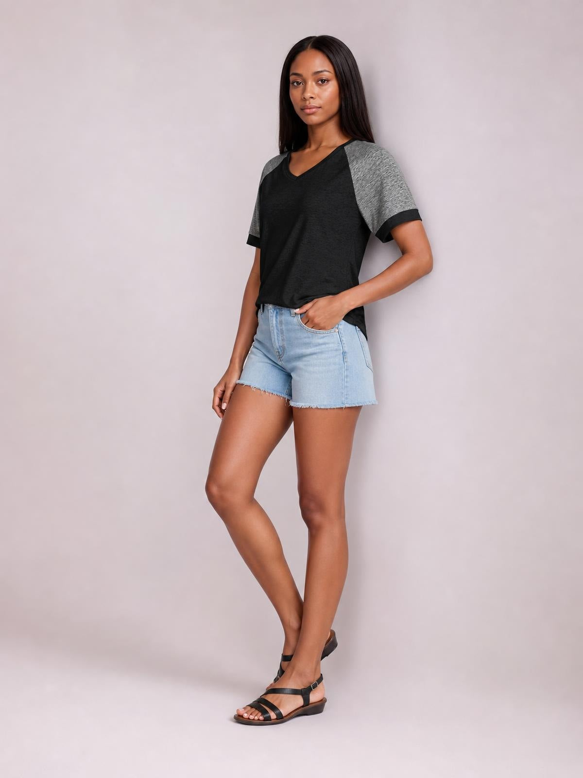 A model poses with one hand in her pocket wearing a black contrast T-shirt with gray short sleeves, black sleeve trim, and a relaxed straight silhouette.