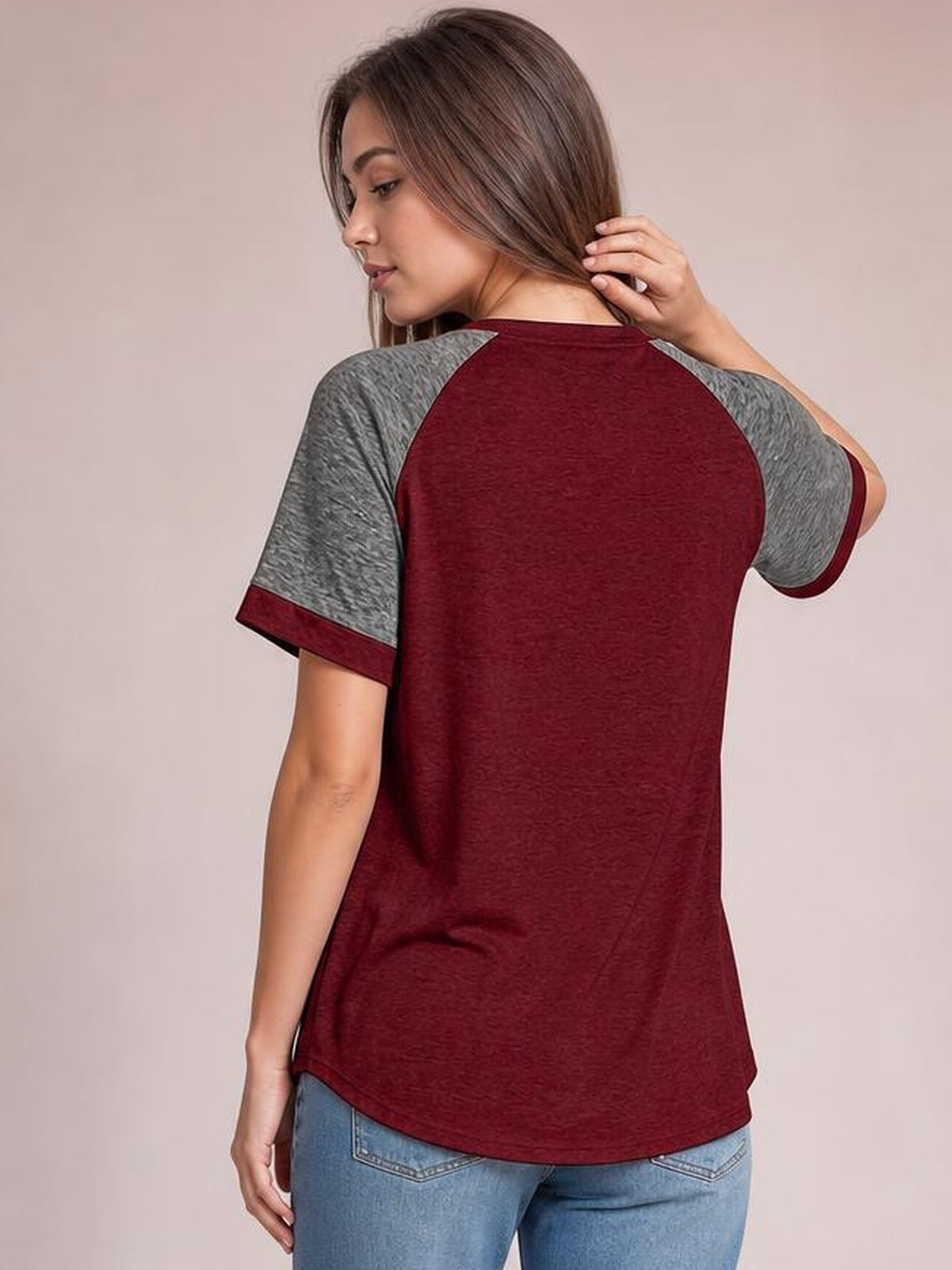 A model poses from the back in a burgundy contrast round-neck short-sleeve T-shirt with gray raglan sleeves, a relaxed silhouette, and curved hem.