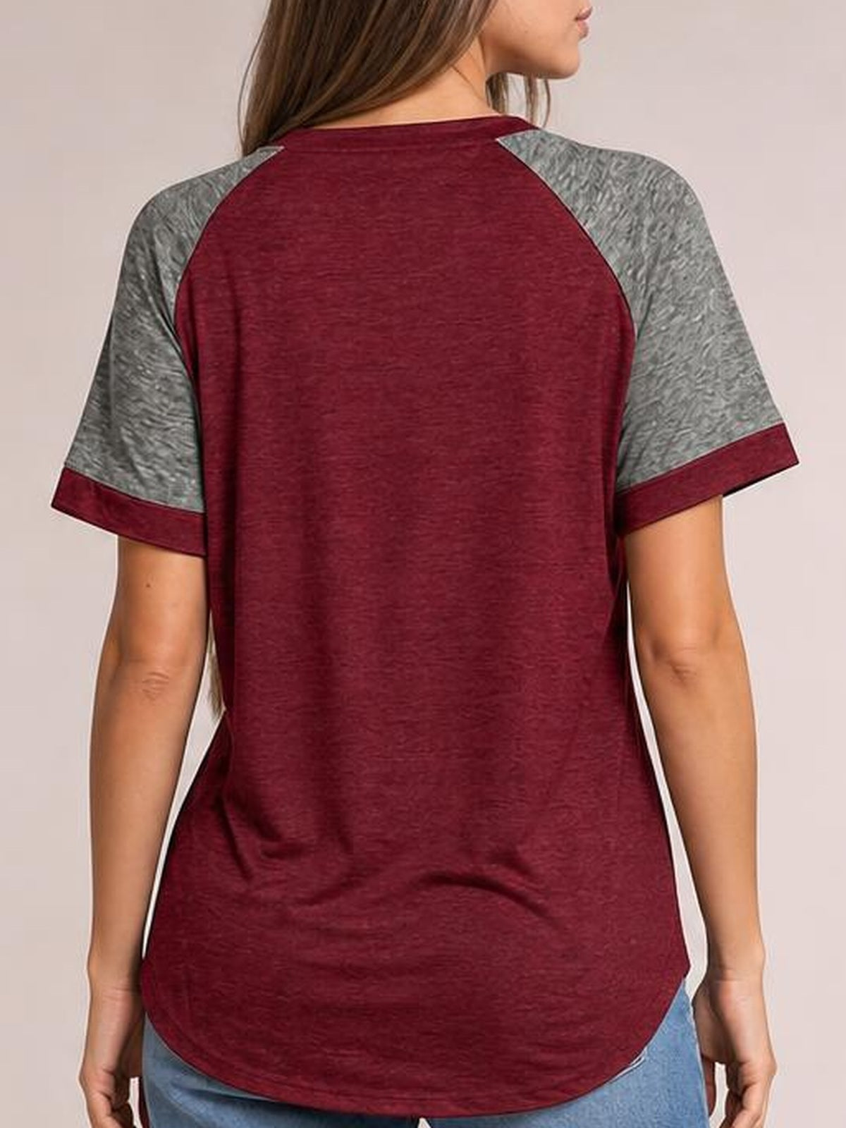 A model stands facing away in a burgundy contrast round neck short sleeve T-shirt with gray sleeves, burgundy cuffs, a relaxed silhouette, and curved hem.