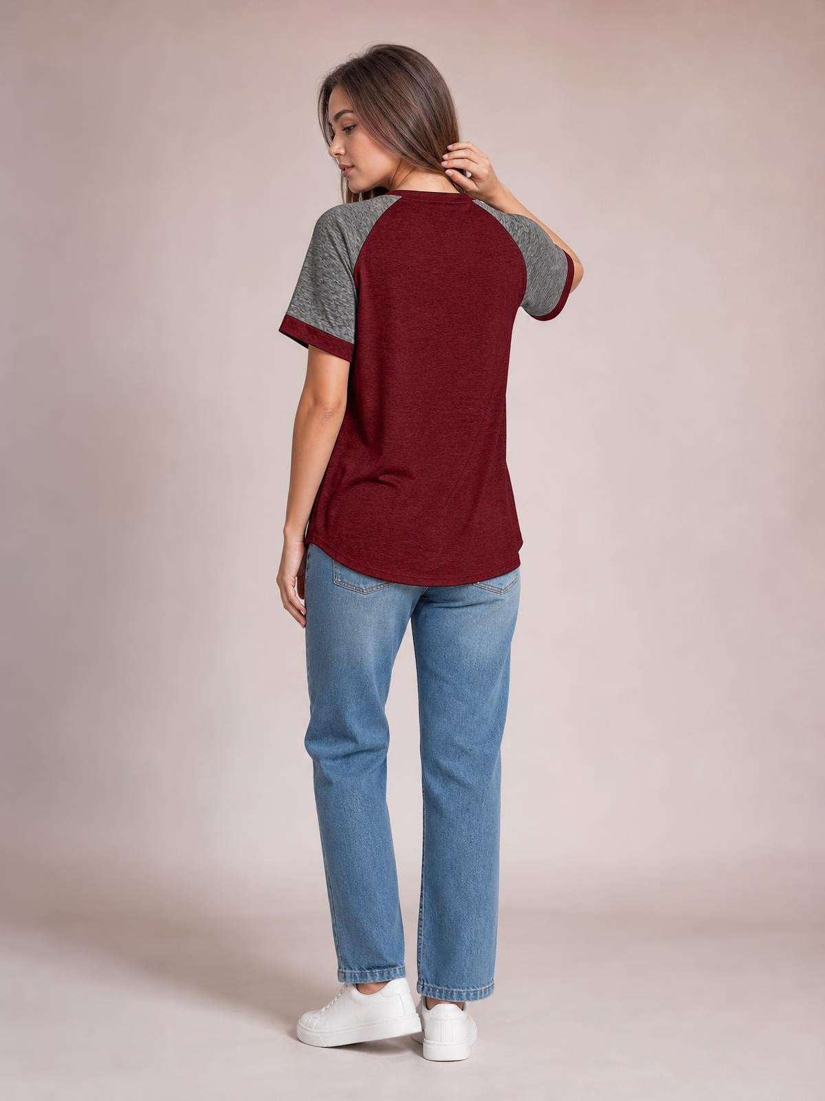 Model shown from behind in a burgundy contrast round-neck short-sleeve T-shirt with gray raglan sleeves and a relaxed, curved-hem silhouette, touching her hair.