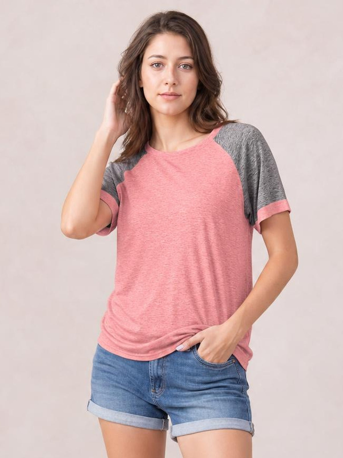Model wearing a pink contrast round neck short sleeve T-shirt with gray sleeves and trim, relaxed straight silhouette, one hand in her shorts pocket.