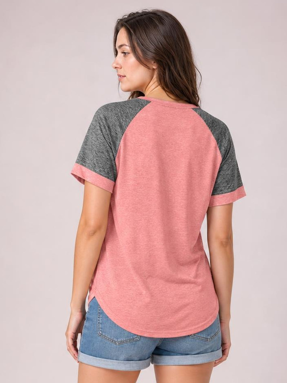 Model viewed from behind wears a pink contrast round neck short sleeve T-shirt with dark gray raglan sleeves, cuffed sleeve hems, and a gently curved relaxed silhouette.