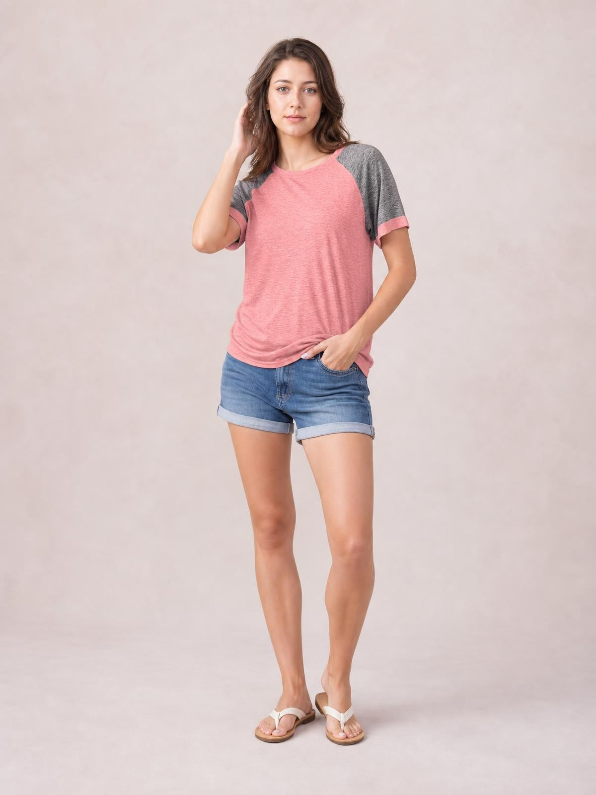 Woman poses with one hand in her pocket wearing a pink contrast round neck short sleeve T-shirt with gray raglan sleeves and a relaxed straight silhouette.