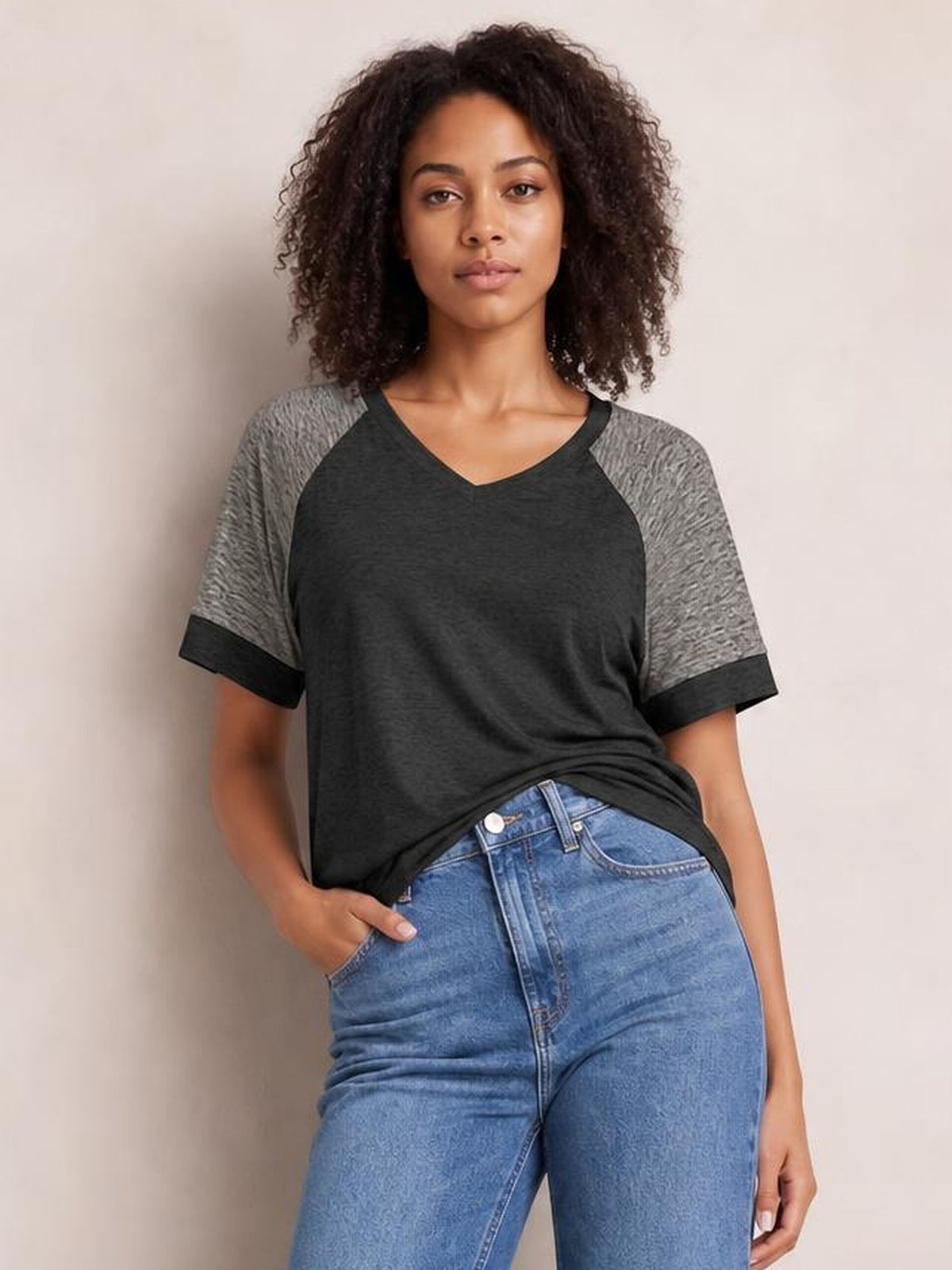 A model poses in a relaxed stance wearing a black contrast short-sleeve T-shirt with gray raglan sleeves, dark trim, and a loose silhouette.
