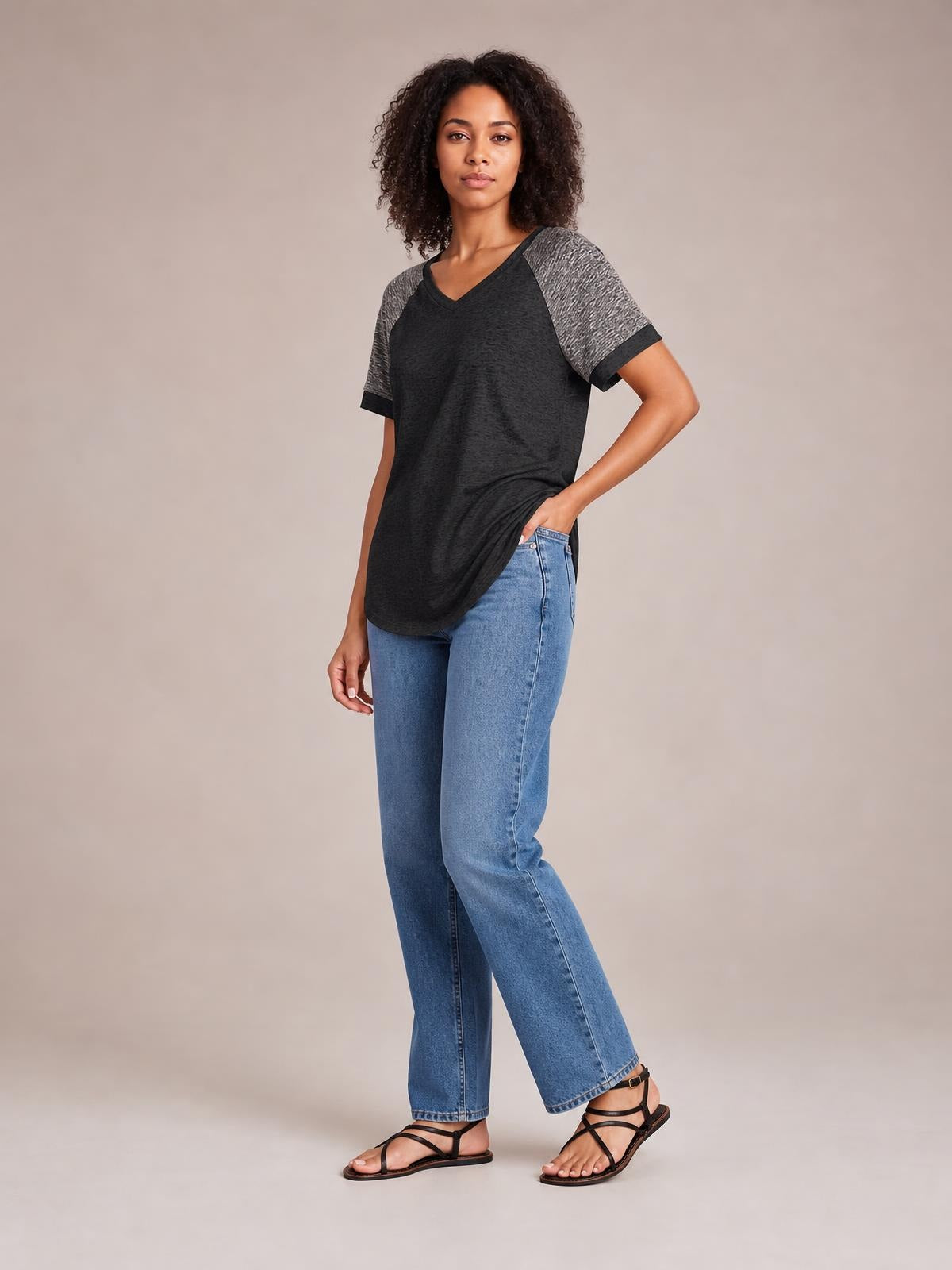 Model wearing a black contrast round neck short sleeve T-shirt with gray sleeves and trim, relaxed tunic silhouette, posing with one hand in her jeans pocket.