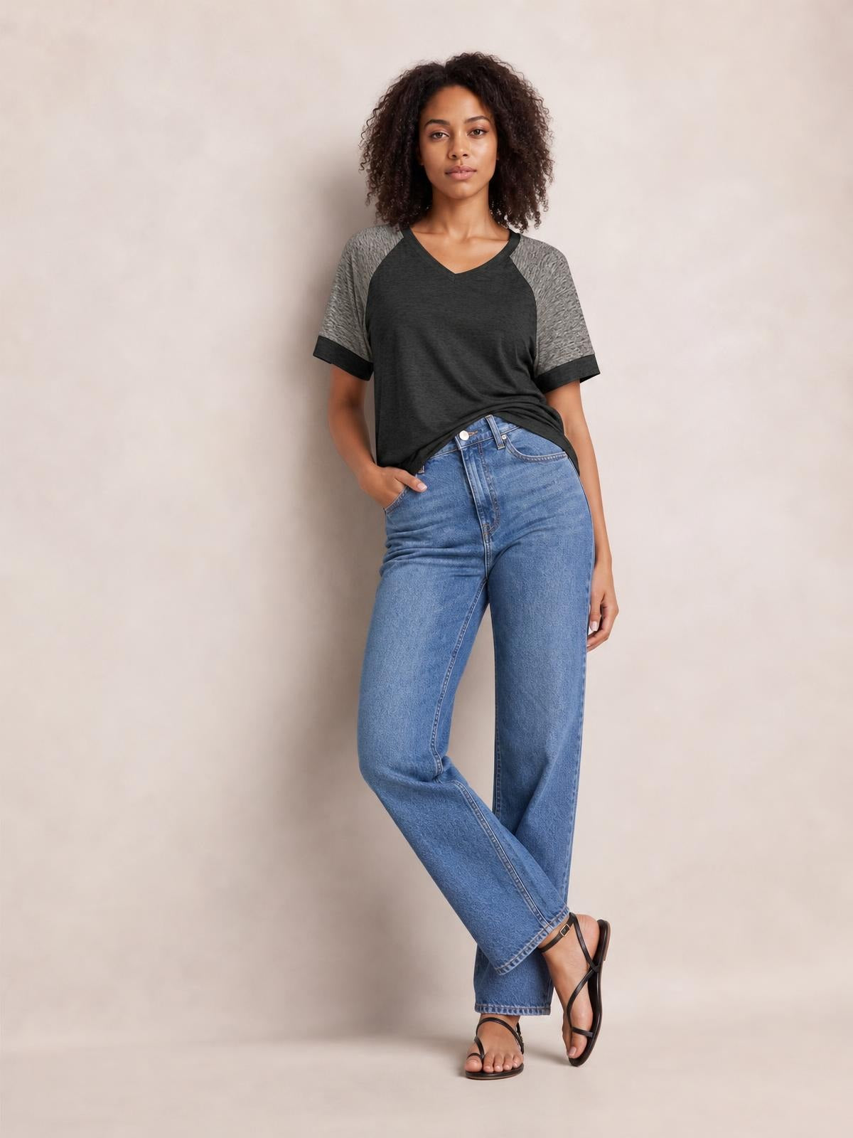 Model wears a charcoal contrast short-sleeve T-shirt with gray raglan sleeves, dark cuffs, and a relaxed silhouette, posing with one hand in her jeans pocket.
