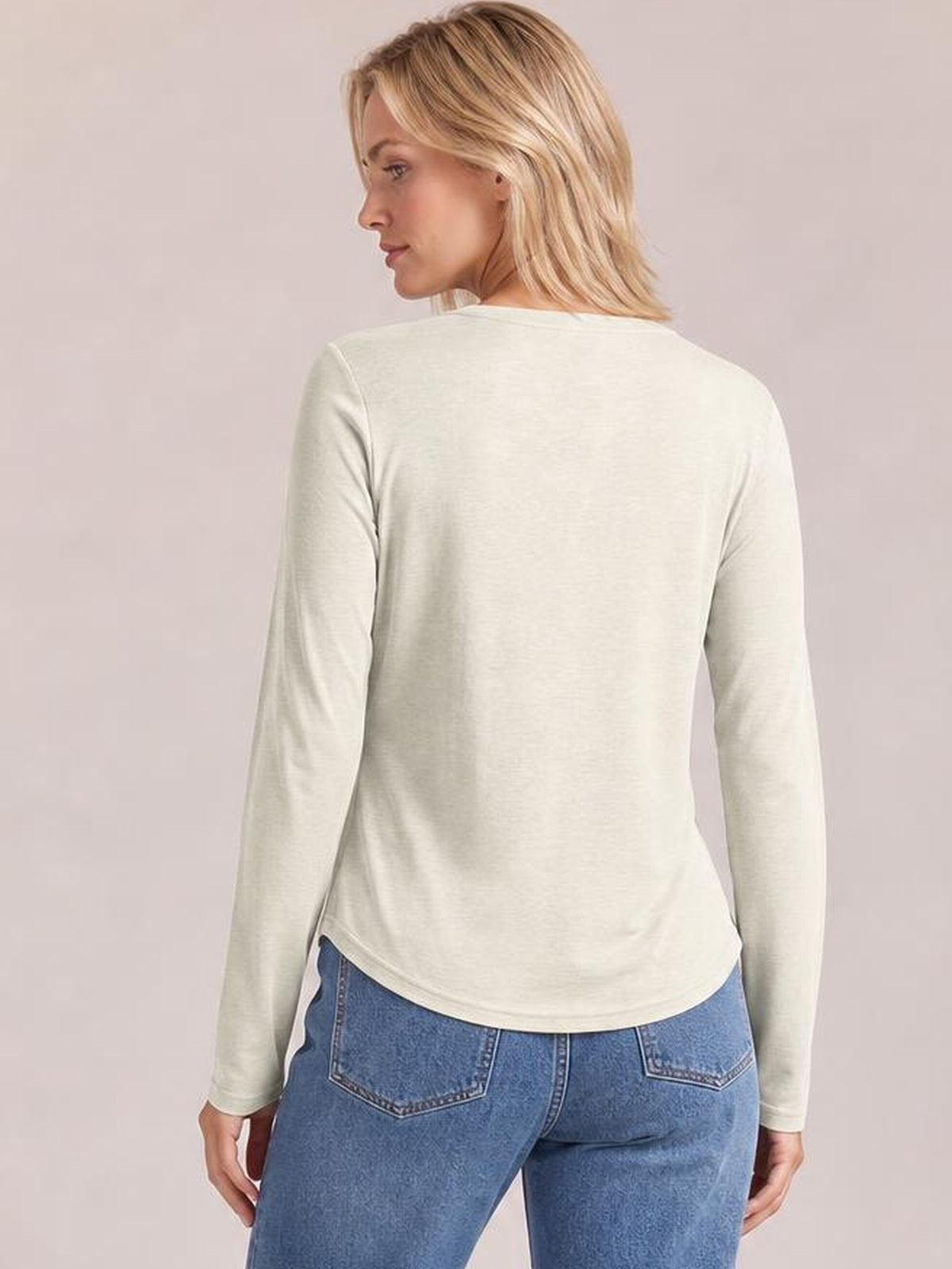 A model looks over her shoulder wearing an opaque cream long-sleeve T-shirt with a smooth back, relaxed silhouette, and rounded hem.