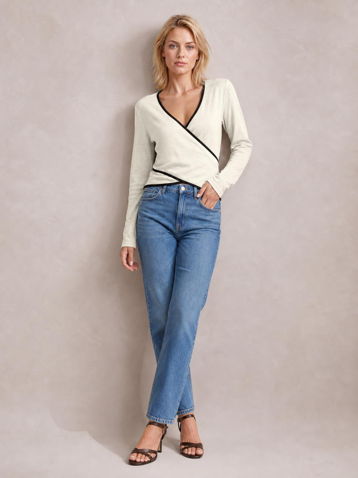 Model in a relaxed pose wears an ivory long-sleeve T-shirt with black contrast trim, a crisscross wrap-style front, and a fitted silhouette.