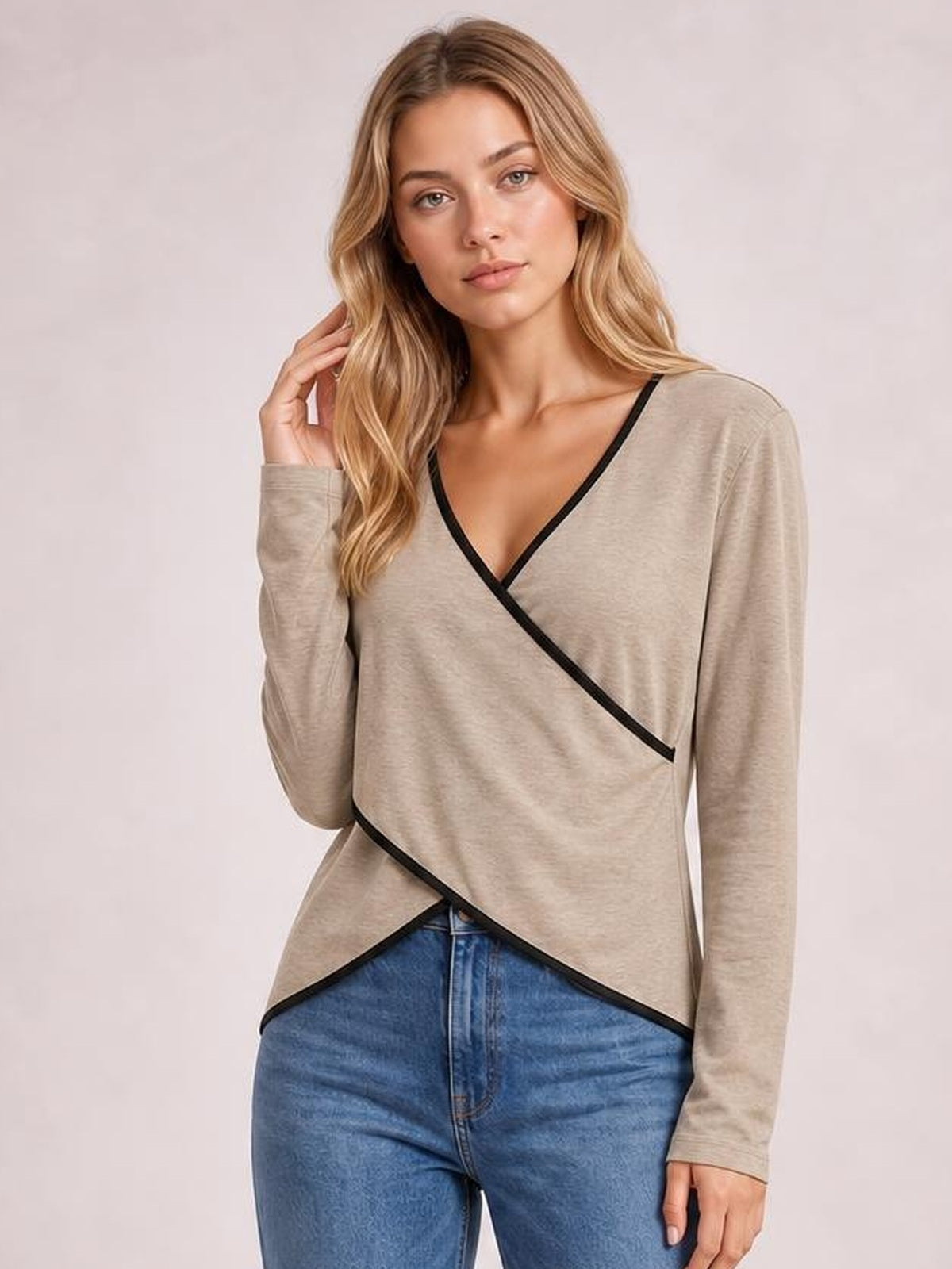 Model poses in a beige long sleeve T-shirt with black contrast trim, crisscross wrap-front construction, V-neckline, and a relaxed asymmetrical silhouette.