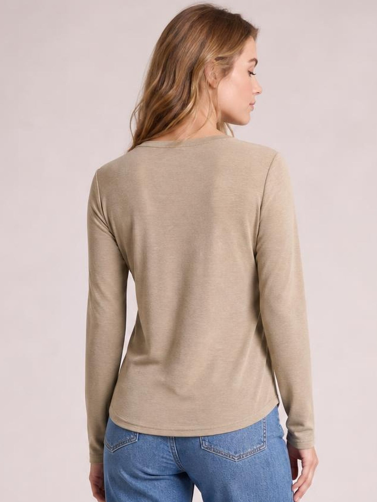 A model shown from behind wears a taupe long-sleeve T-shirt with a round neckline, relaxed silhouette, and slightly curved hem.