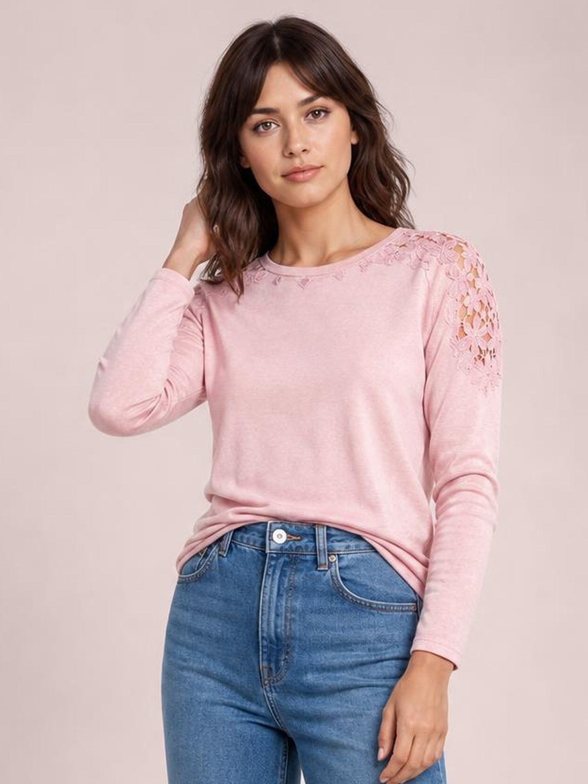 A woman poses in a soft pink round-neck long-sleeve T-shirt with lace cutout detailing along the shoulders and upper sleeves in a relaxed silhouette.