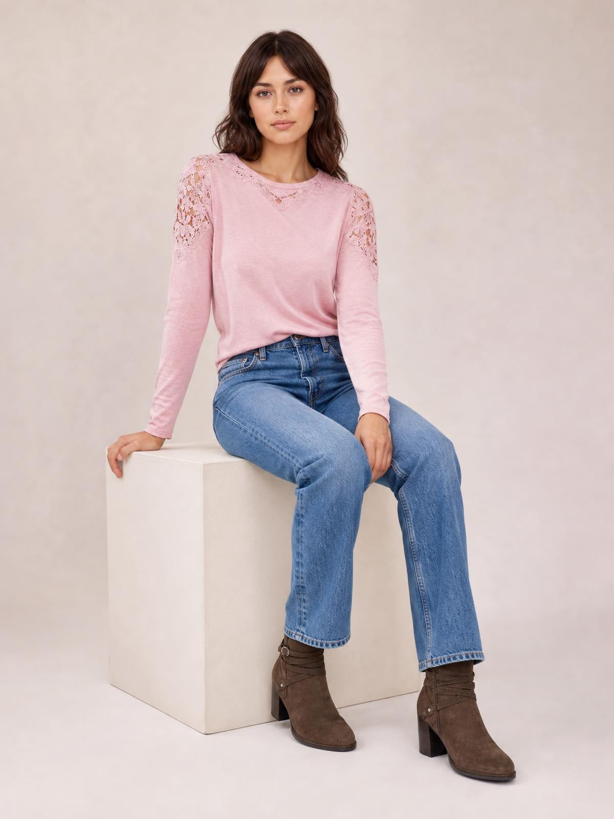 Model seated in a pink cutout round neck long sleeve T-shirt with lace-detail shoulders and a relaxed silhouette.