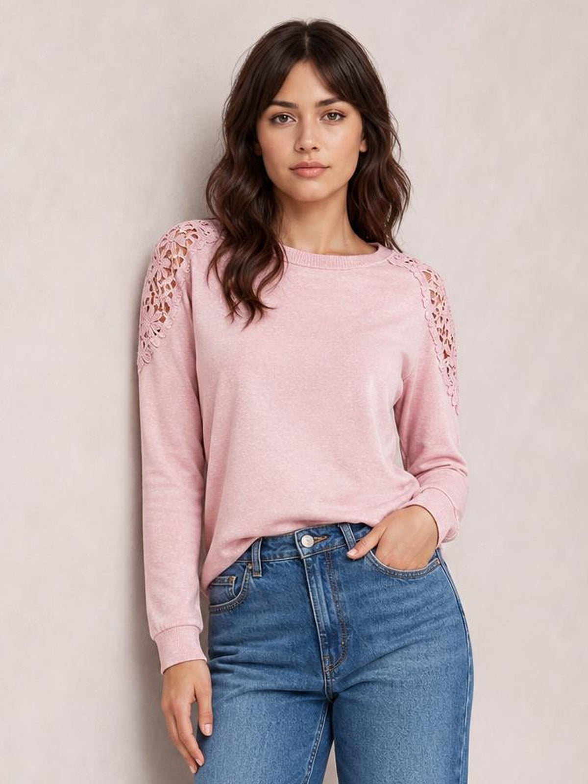 Model wears a pink cutout round neck long sleeve T-shirt with lace shoulder details, ribbed cuffs, a relaxed silhouette, and one hand in her jeans pocket.