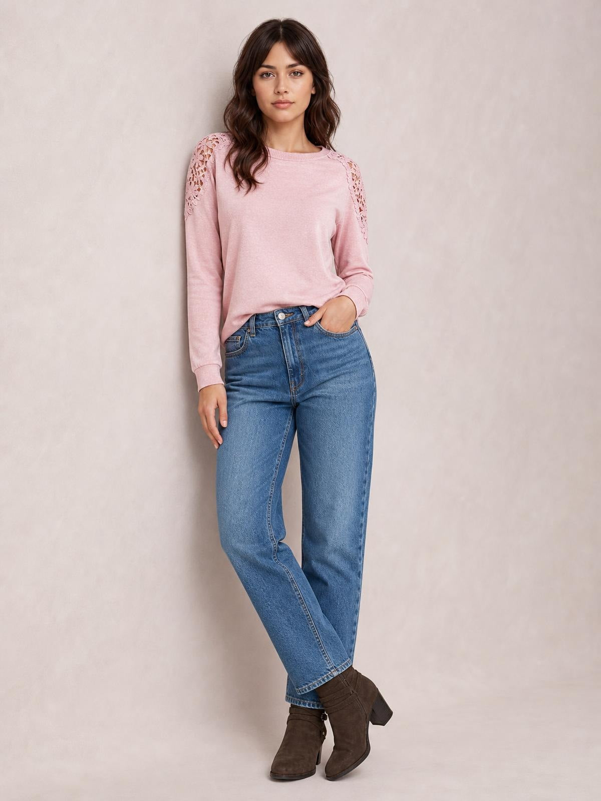 Model wears a pink cutout round-neck long-sleeve T-shirt with lace shoulder details and a relaxed silhouette, standing with crossed legs and one hand in her jeans pocket.