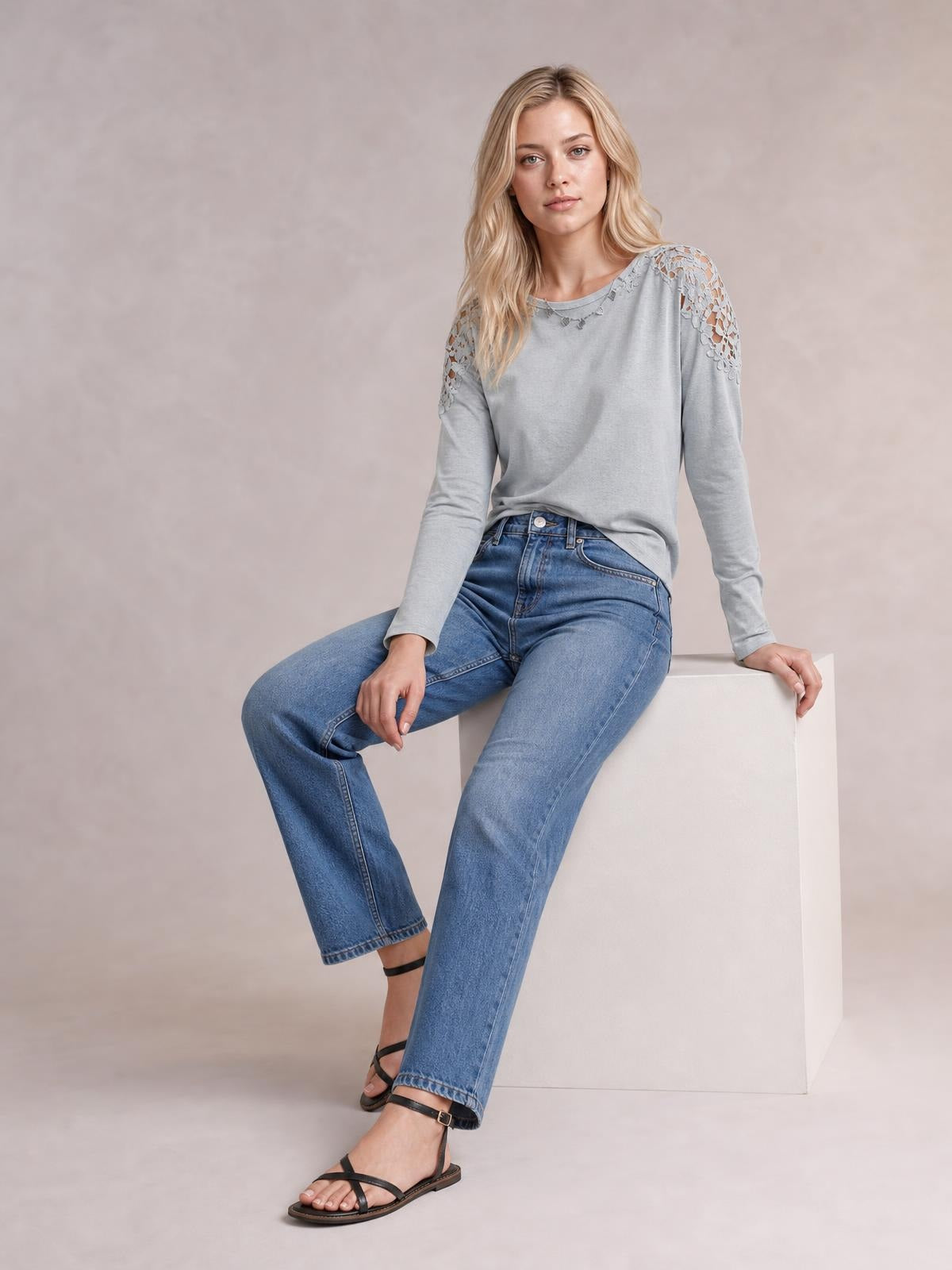 Model seated in a light gray cutout round neck long sleeve T-shirt with semi-sheer floral lace shoulder panels and a relaxed silhouette.
