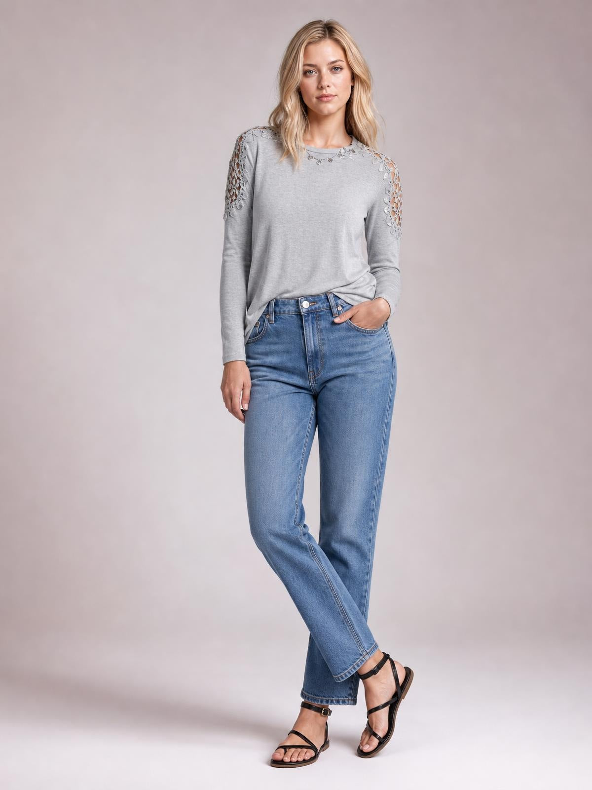 Model wears a gray cutout round neck long sleeve T-shirt with lace-detail shoulder panels and a relaxed silhouette, posing with one hand in her jeans pocket.