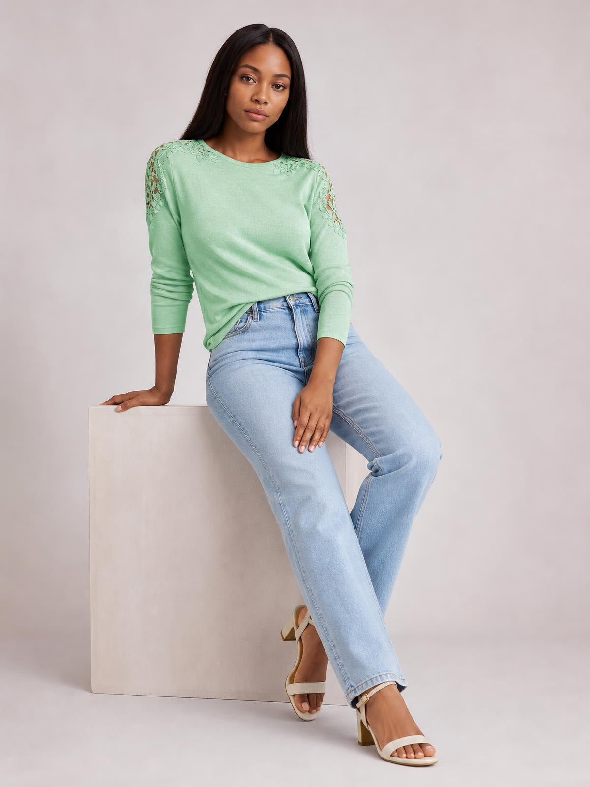 Model seated in a mint green cutout round neck long sleeve T-shirt with lace details at the shoulders and sleeves, shown in a relaxed silhouette.